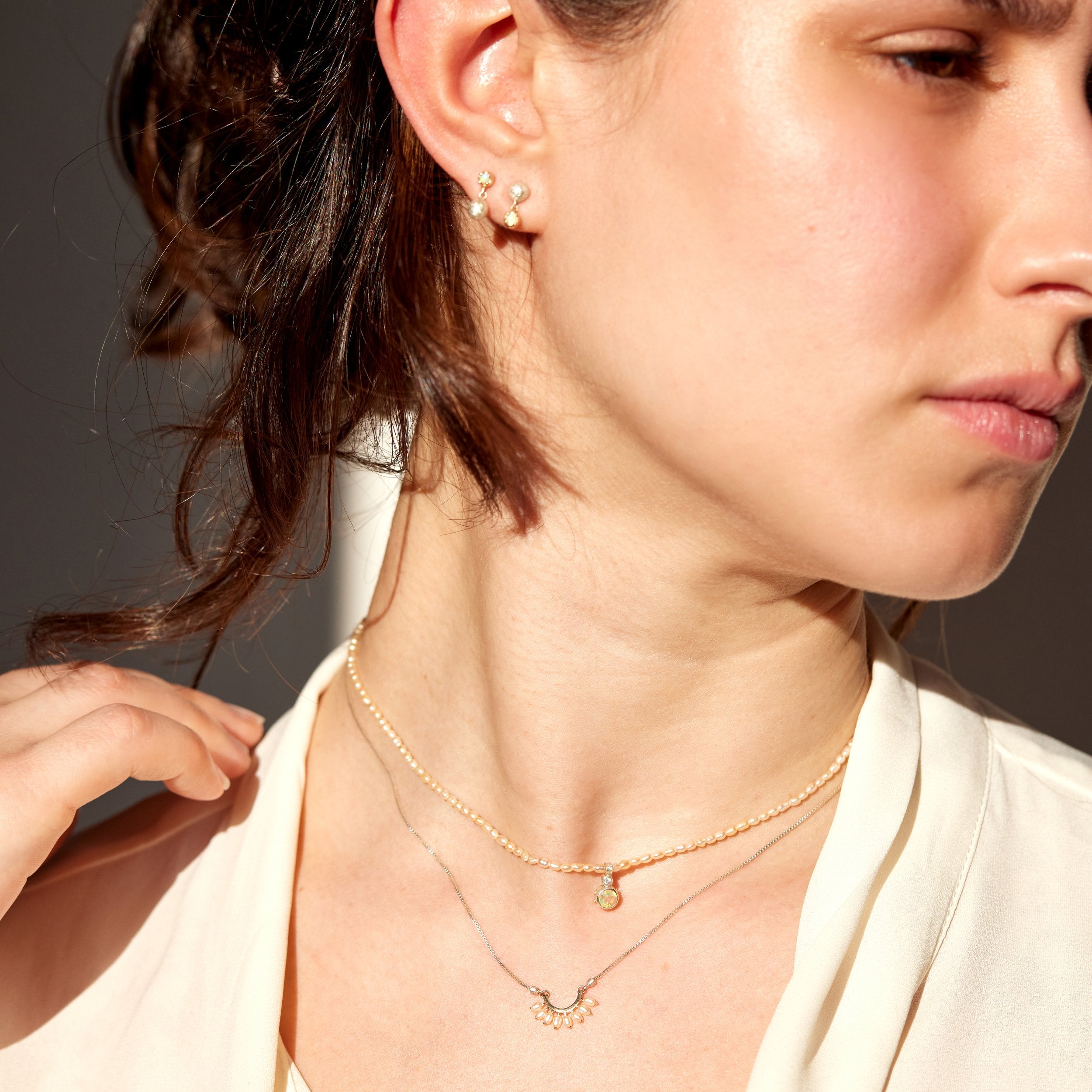 Close-up of a woman wearing gold necklaces and earrings against a neutral background