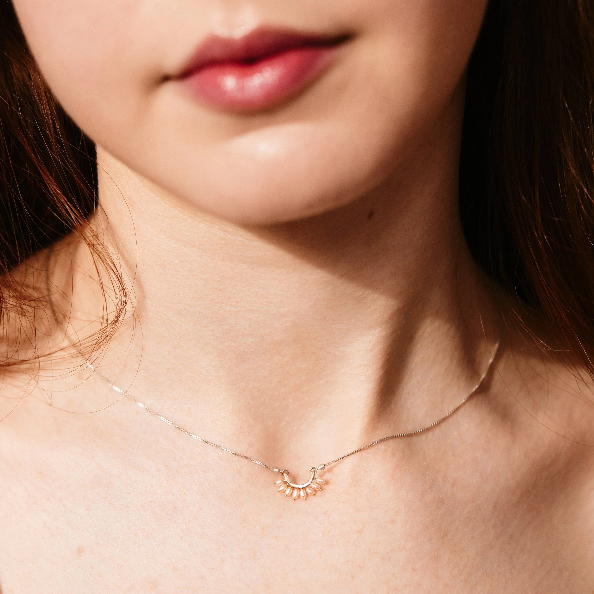 Close-up of a woman wearing a delicate gold necklace with a small pendant.