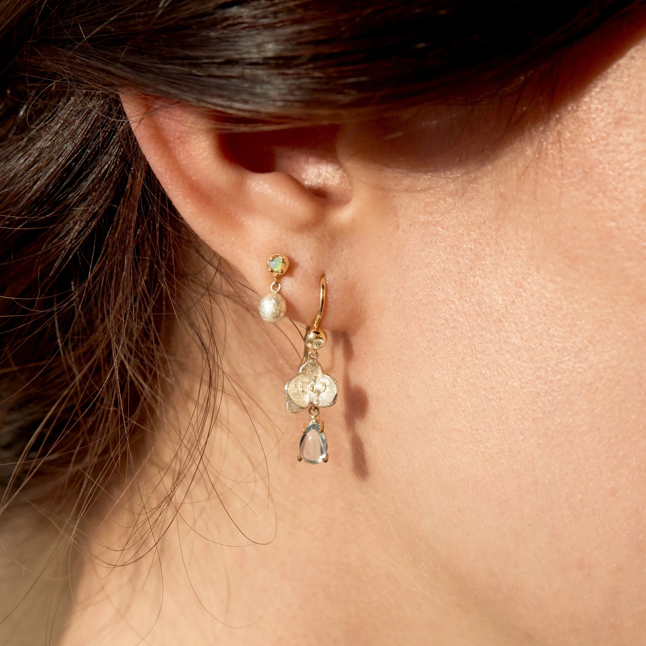 Close-up of a person wearing gold earrings with gemstones.