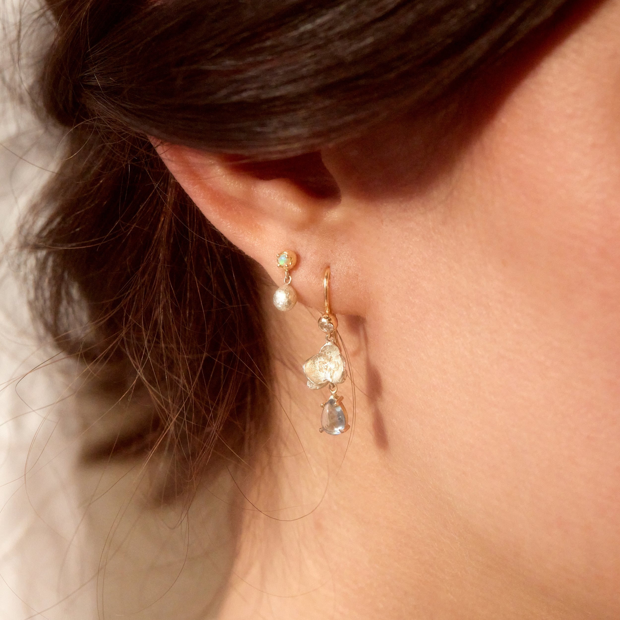 Close-up of an ear wearing a gold earring with a small floral and gemstone detail.