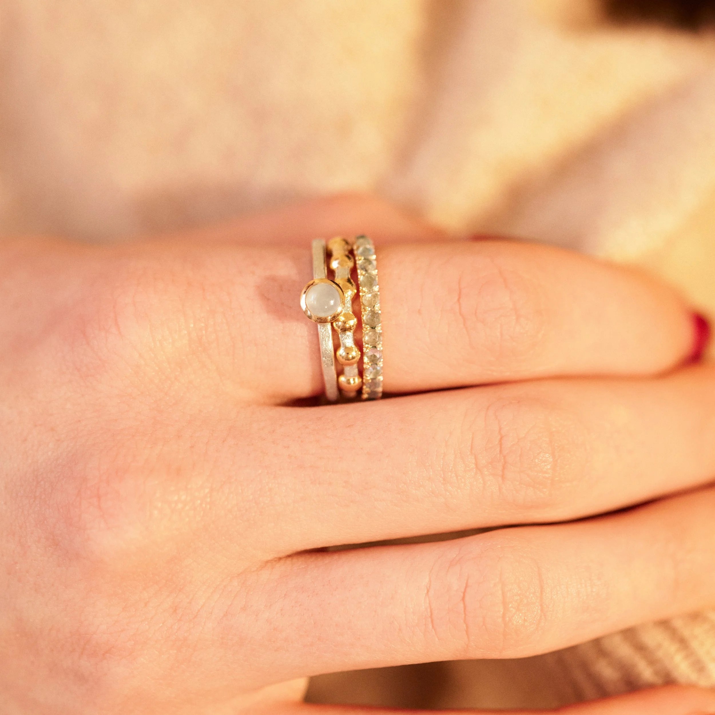 Close-up of a hand wearing three gold rings with gemstones on a blurred background