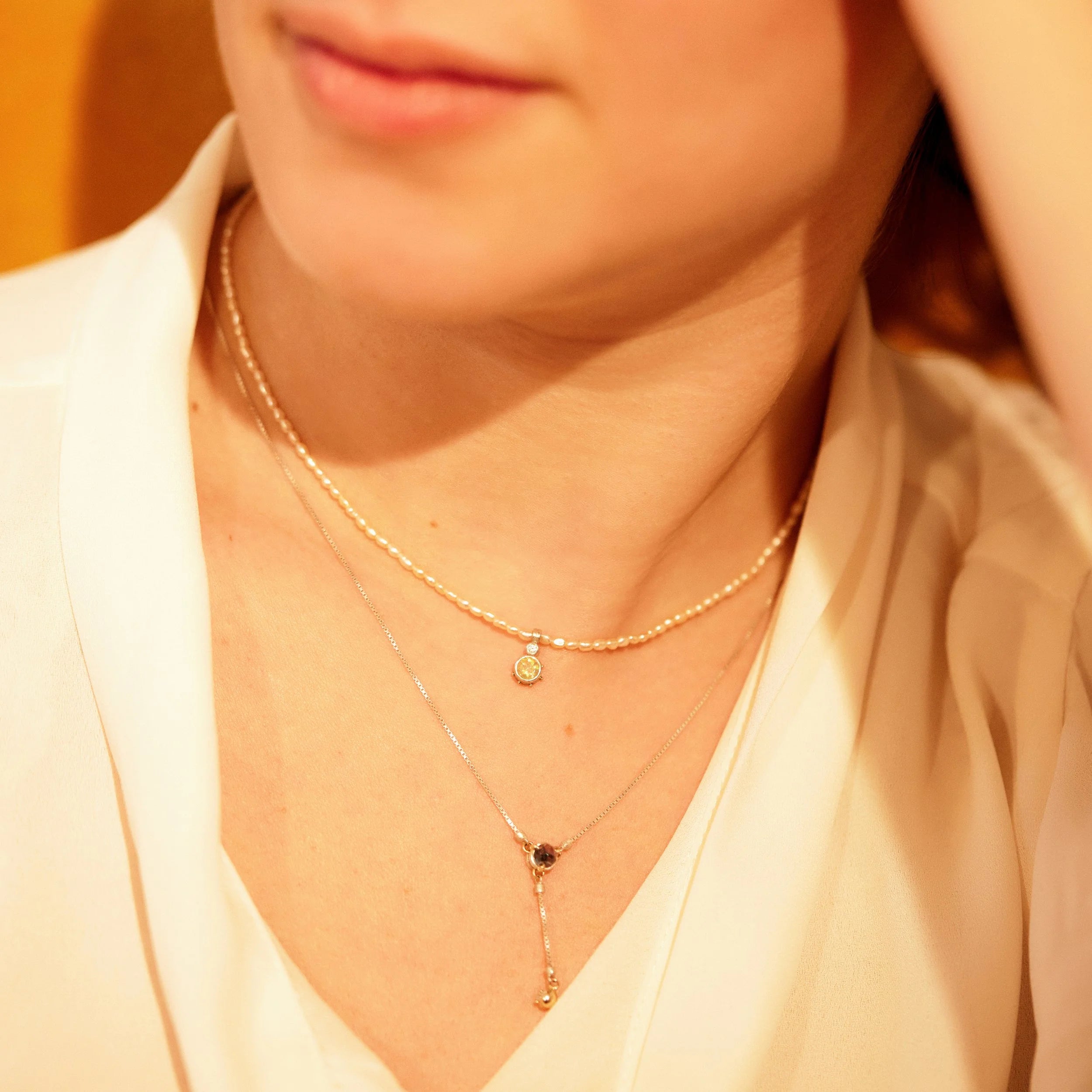 Close-up of a person wearing two gold necklaces with small pendants.