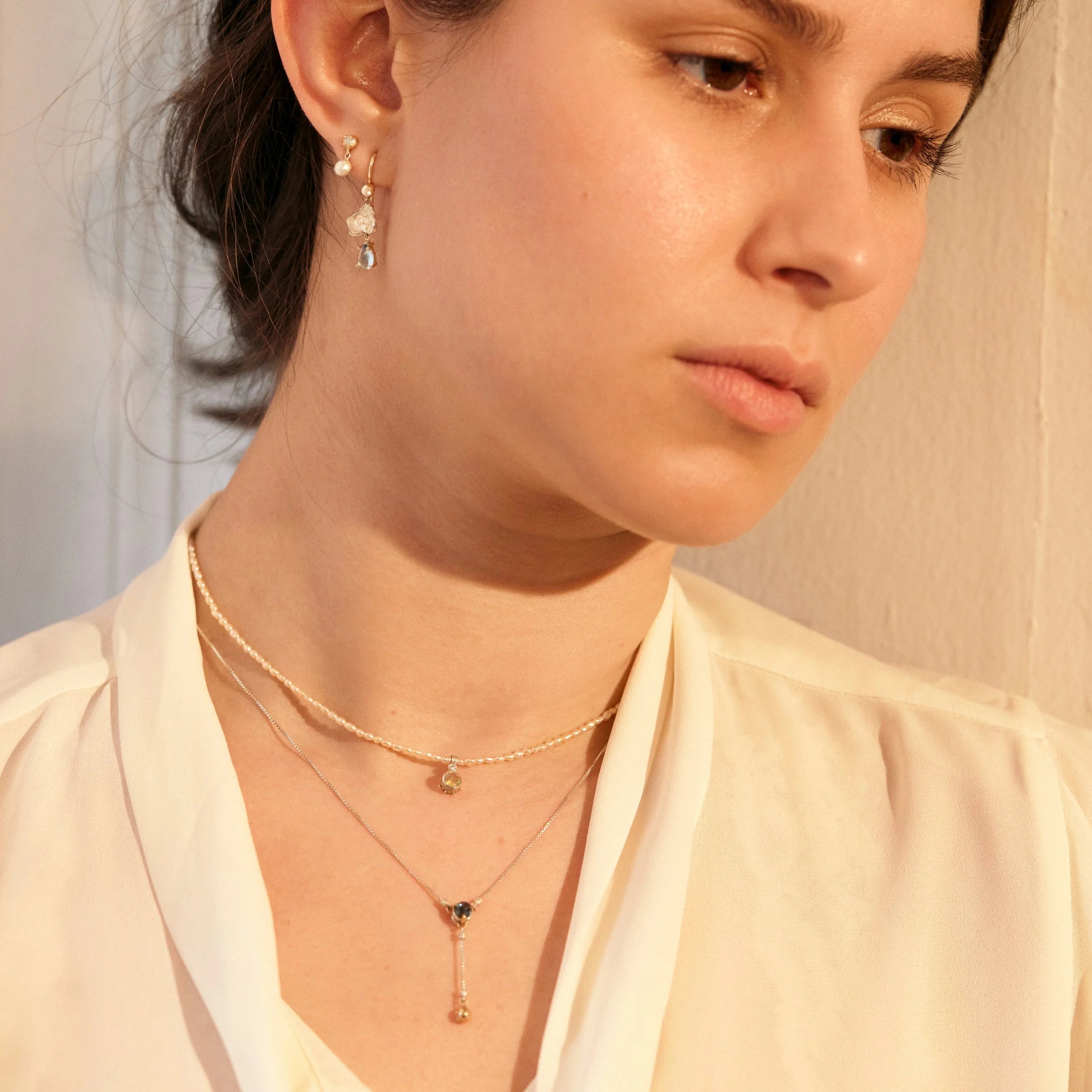 Close-up of a person wearing gold necklaces and earrings against a neutral background