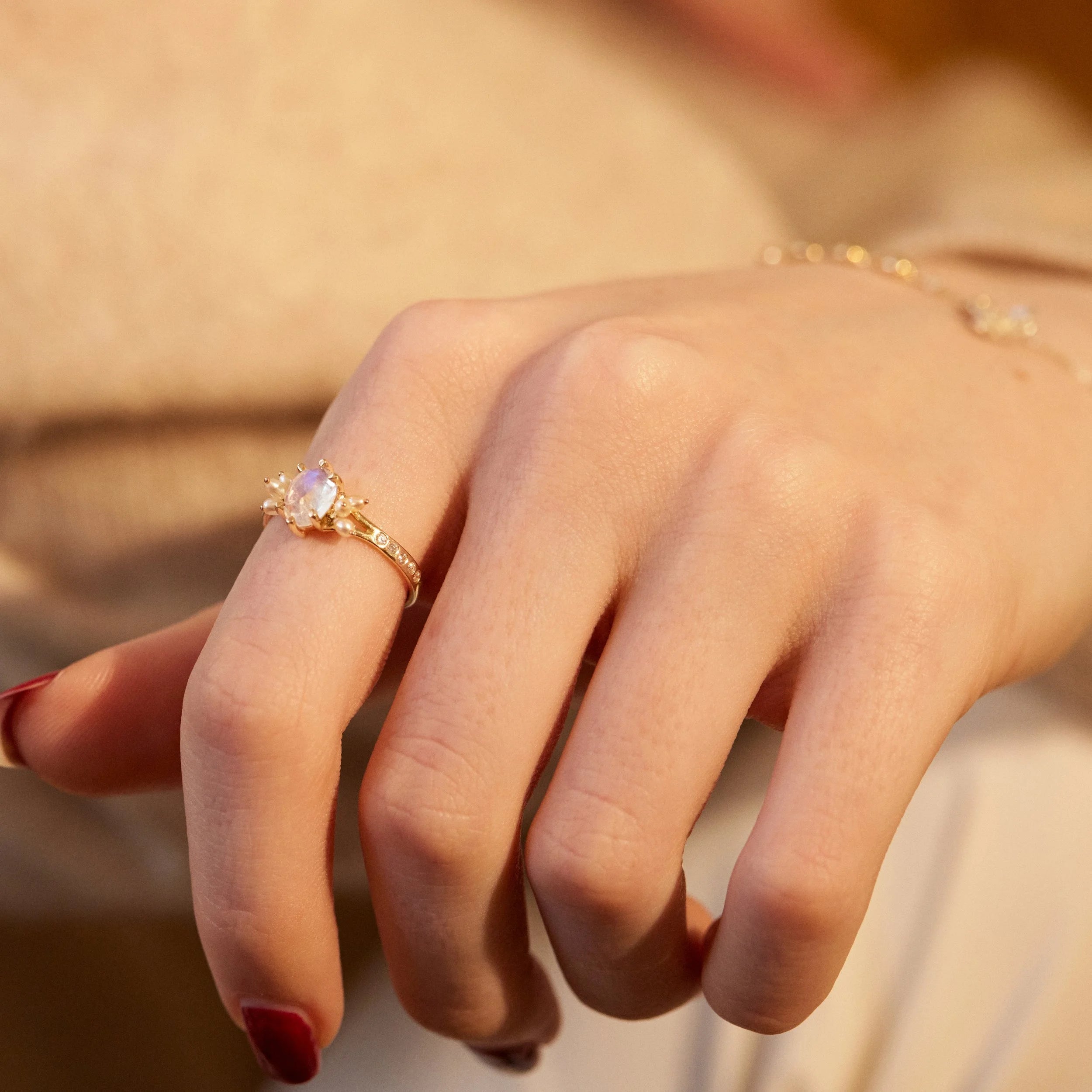 Close-up of a hand wearing a gold ring with a pink stone against a blurred background
