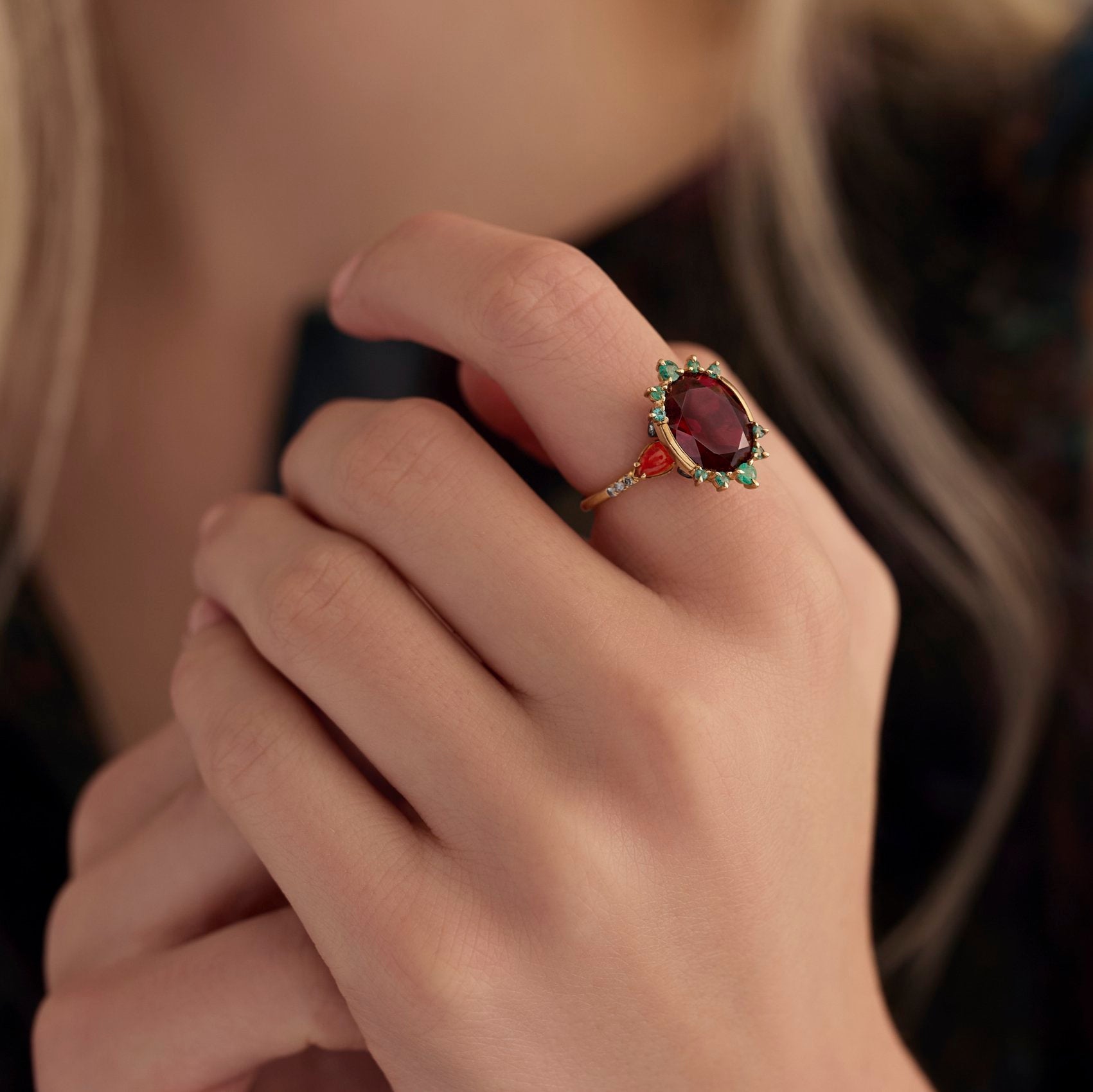 A close-up of a person's hand wearing a vintage-style ring with an oval red gemstone and green accents on a gold-toned band.
