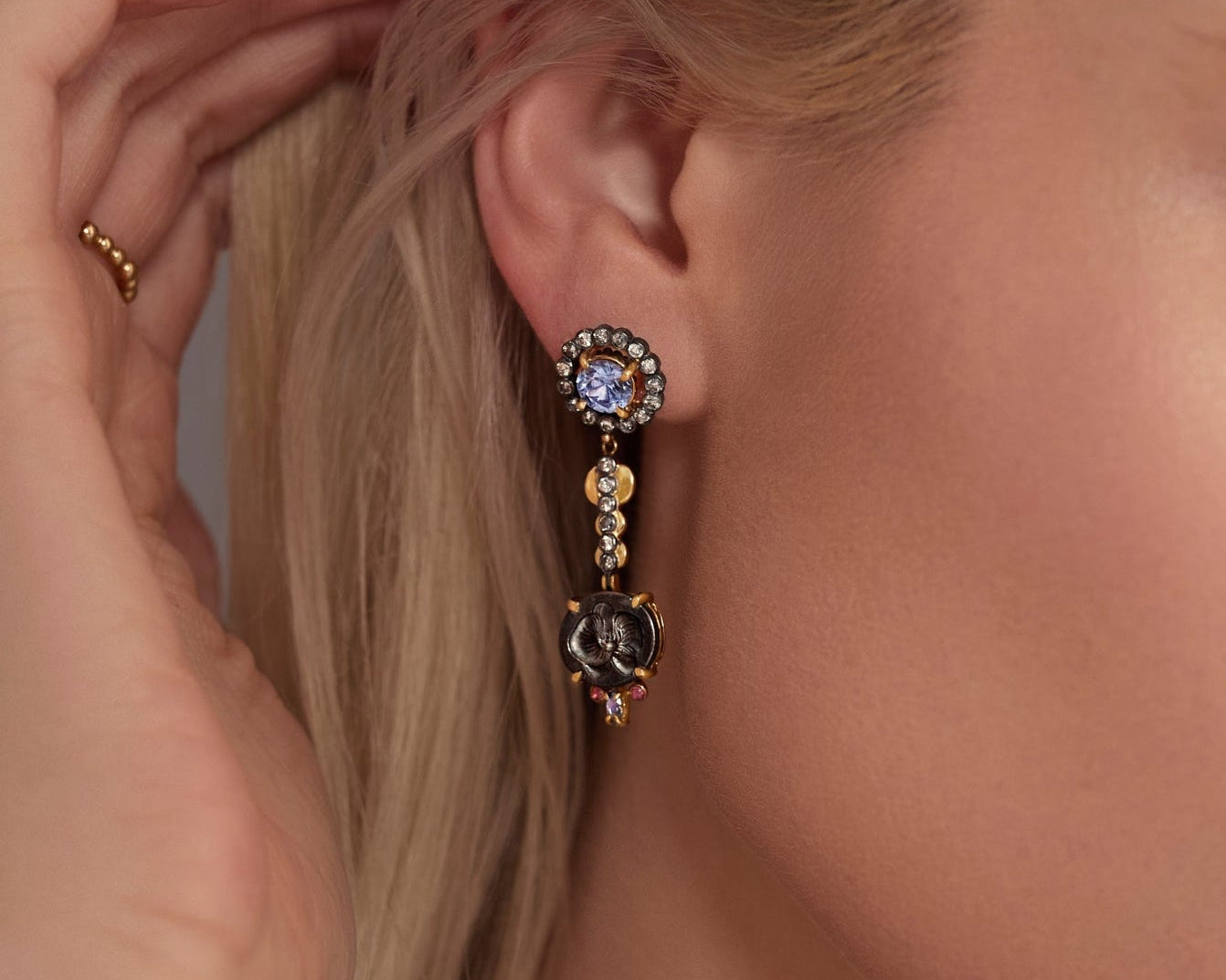 Close-up of a woman wearing an elegant earring with a hand adjusting her hair.