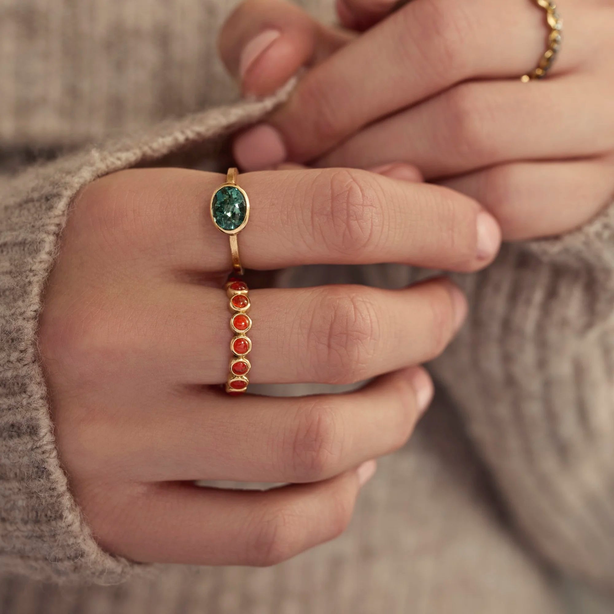 Close-up of a hand wearing two gold rings with gemstones.