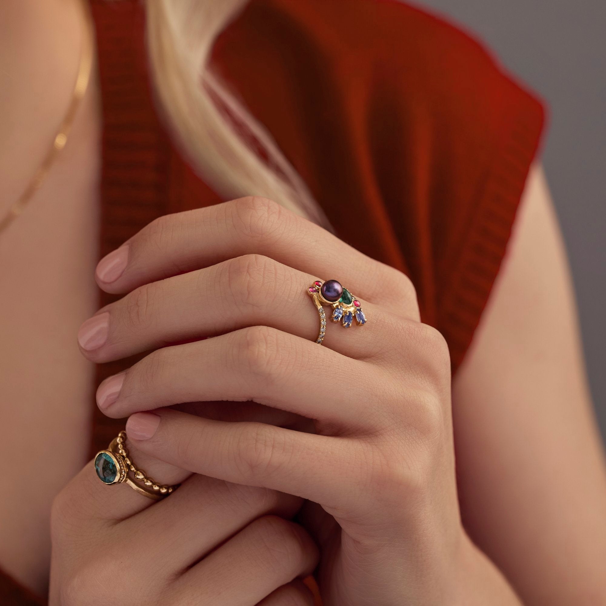 Close-up of hands wearing gold rings with gemstones against a neutral background