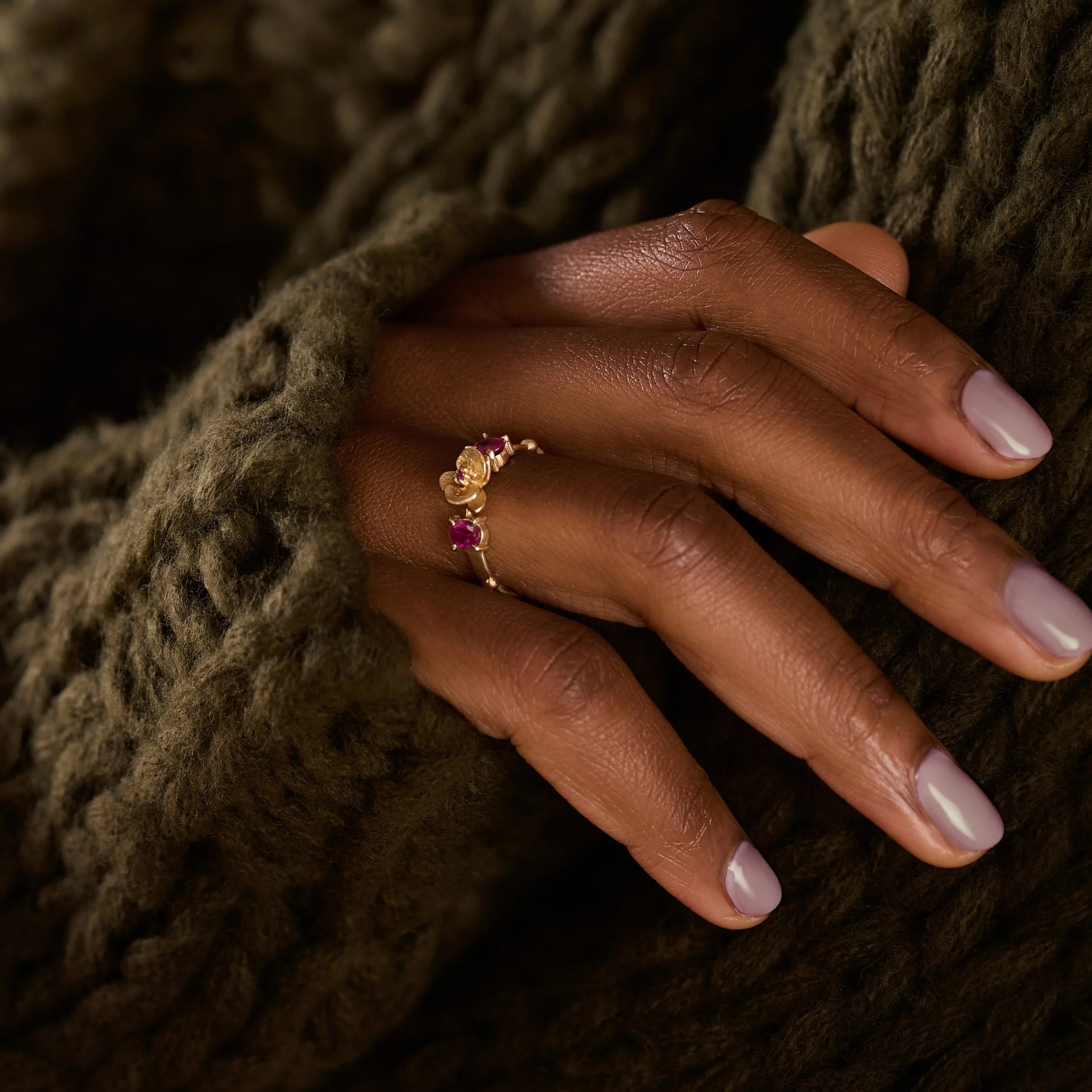 Hand wearing a gold ring with a pink gemstone against a textured brown background