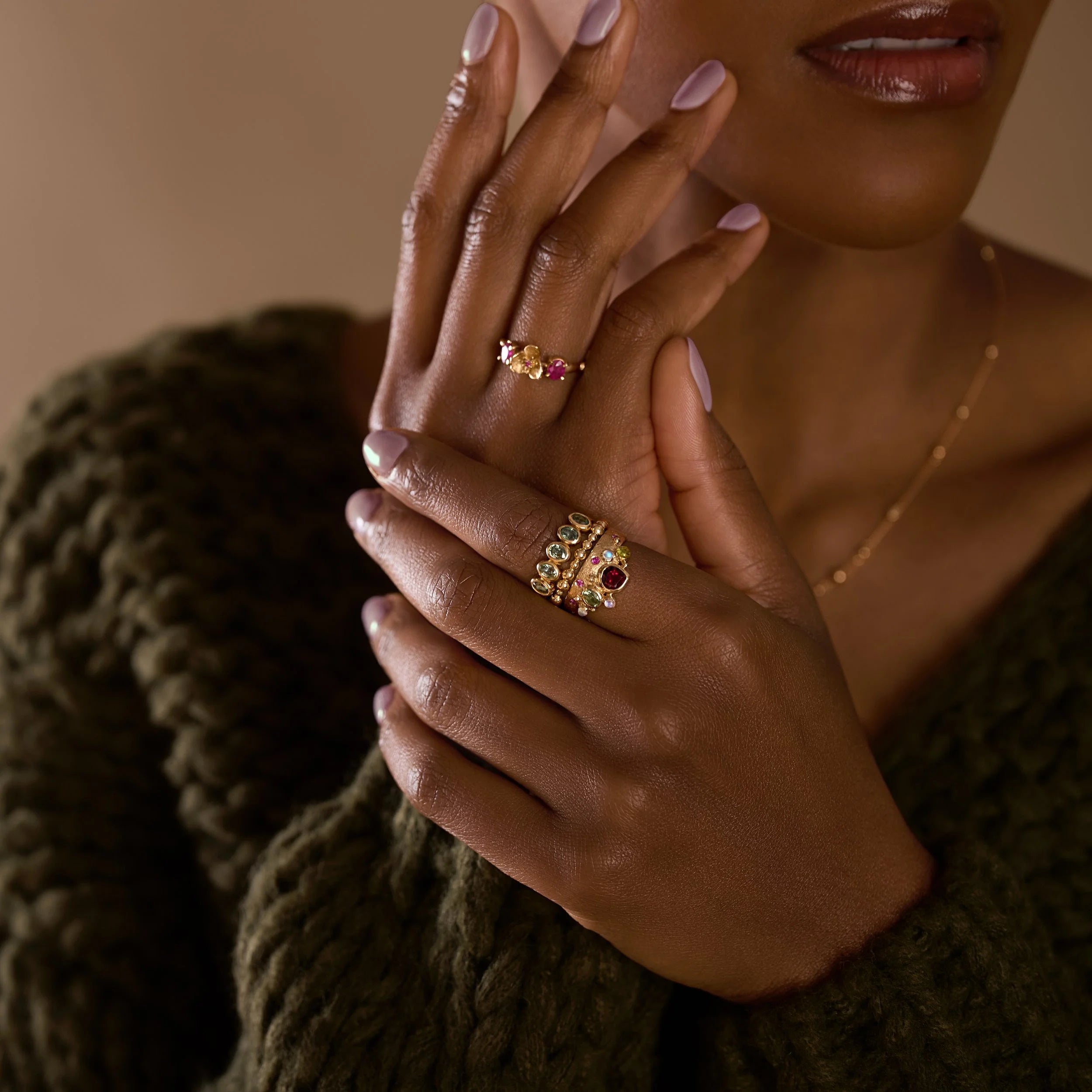 Close-up of a person's hand wearing multiple gold rings with gemstones against a blurred background.