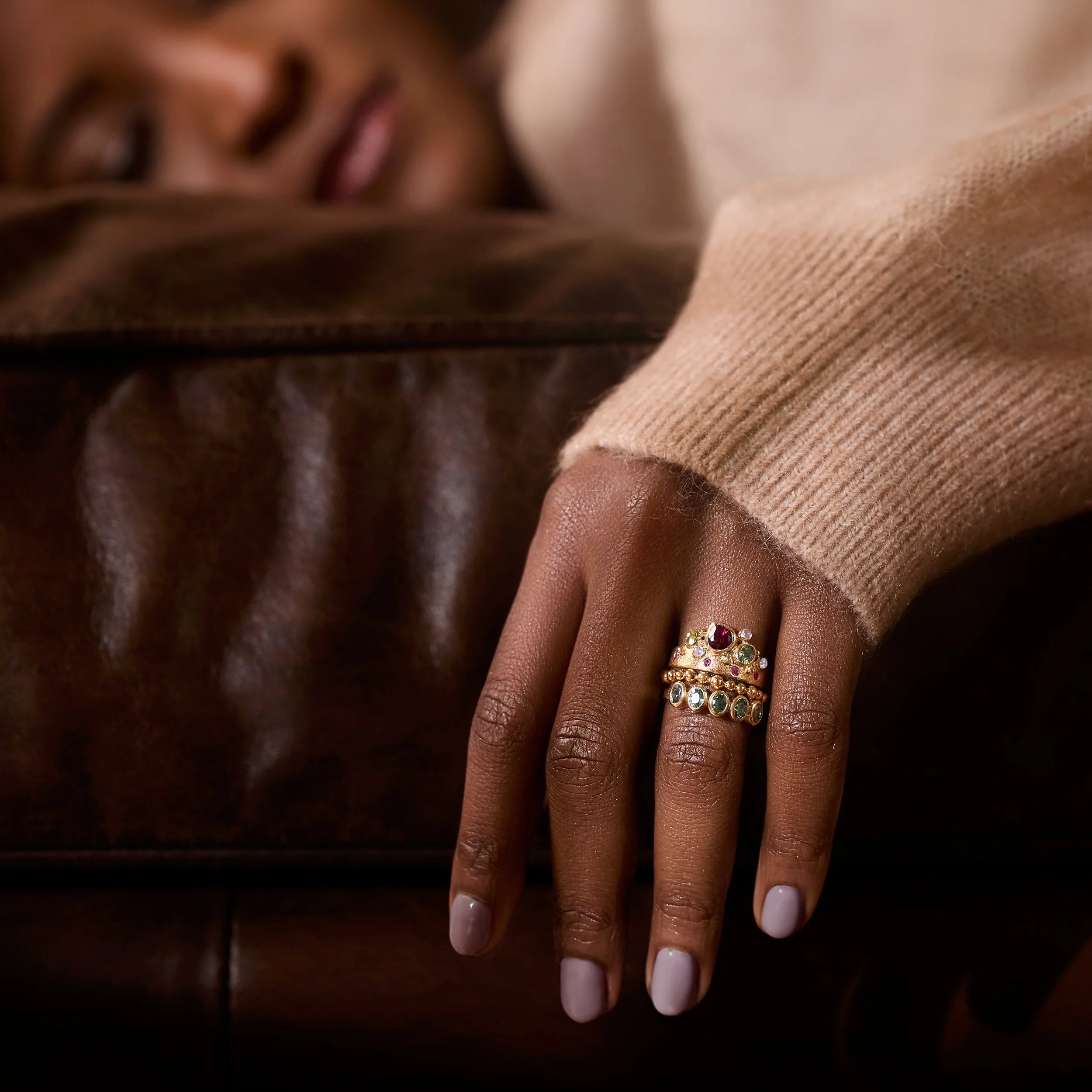 Hand wearing multiple rings with gemstones on a brown leather surface