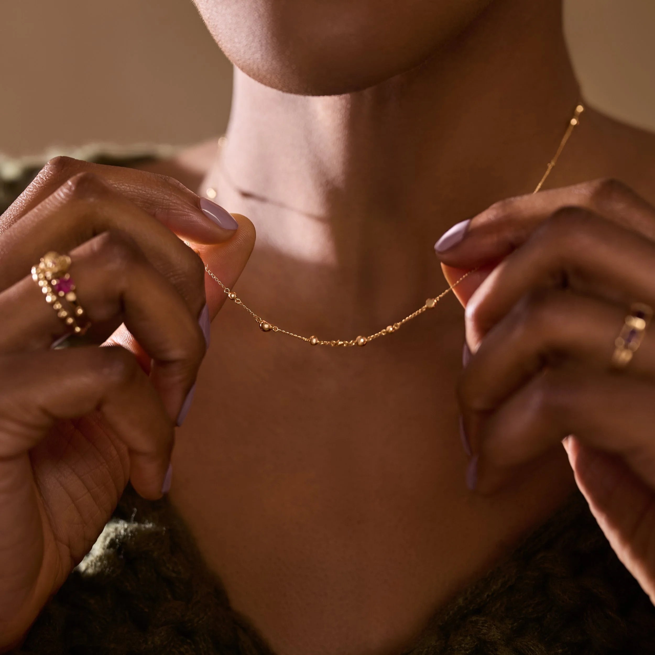 Person wearing a delicate gold necklace with a blurred background