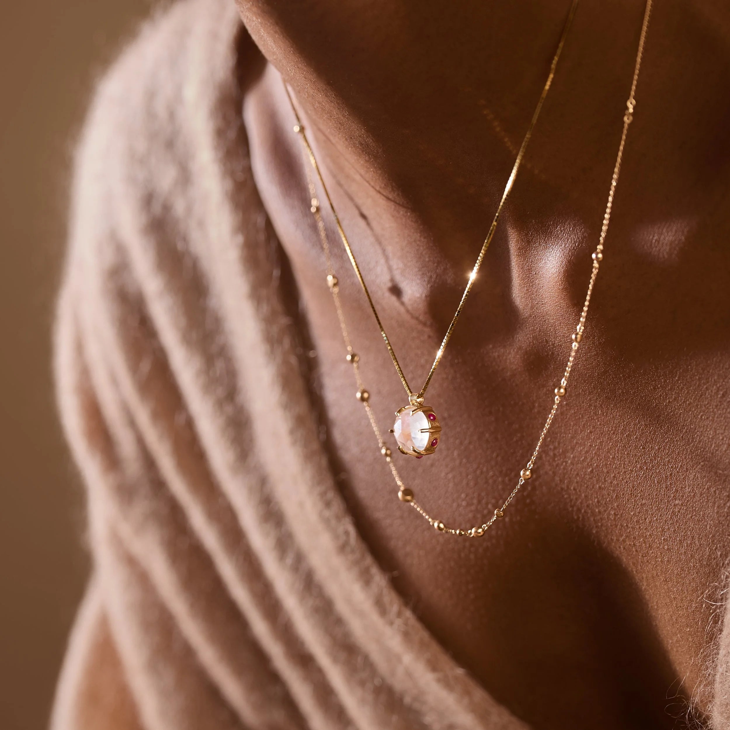 Gold necklace with a pendant draped over a person's neck against a brown background