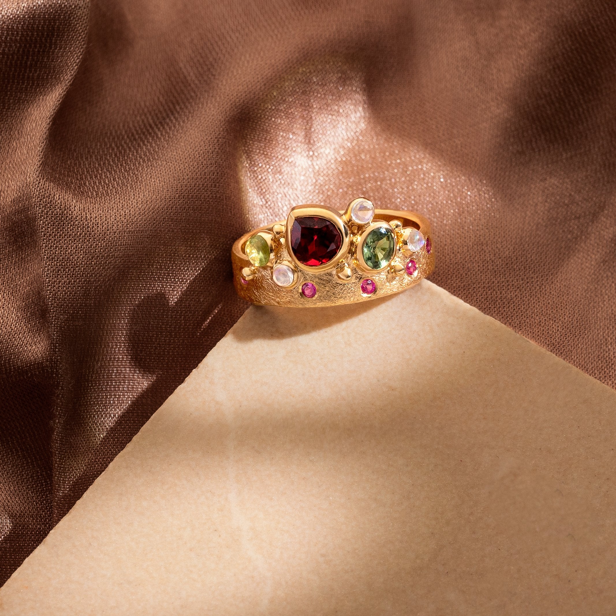Gold ring with multicolored gemstones on a brown fabric background