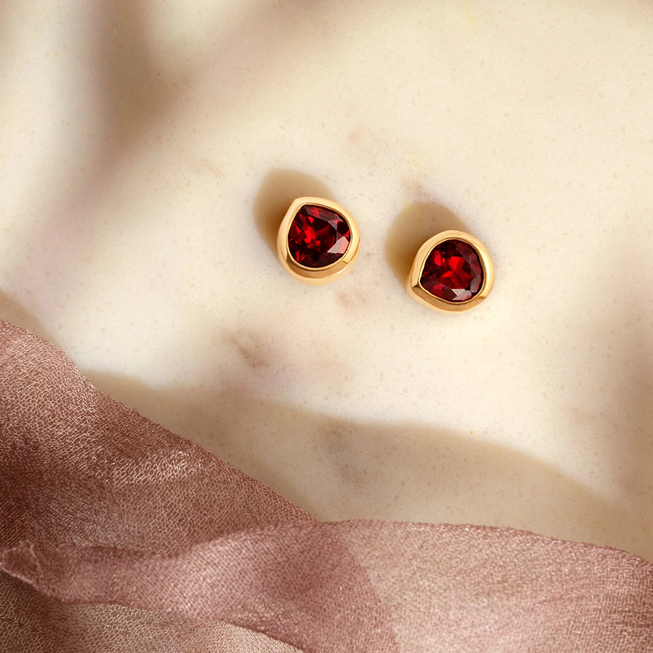 Gold earrings with red gemstones on a beige fabric background