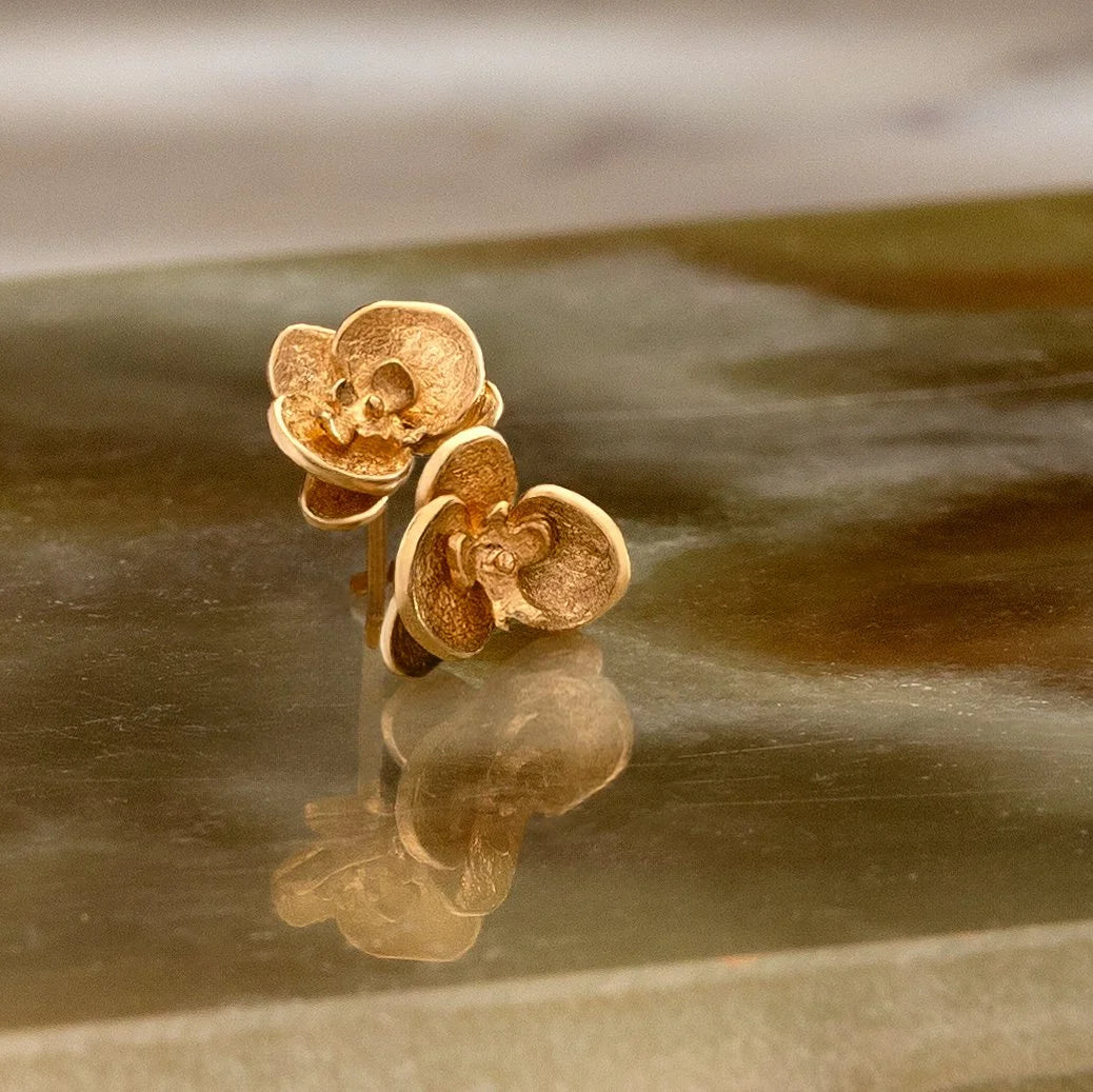 Gold flower-shaped earrings on a reflective surface