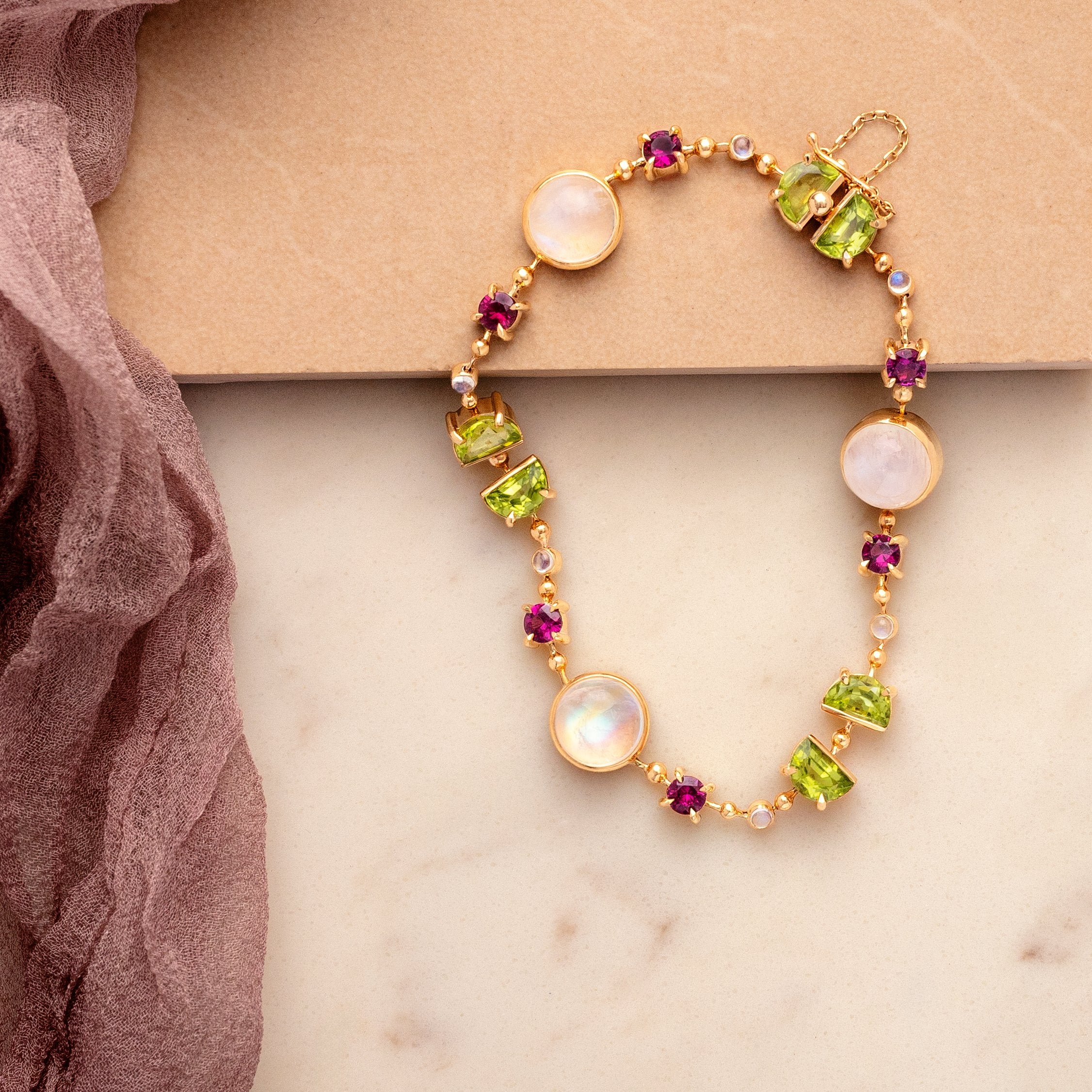 Gold bracelet with gemstones on a beige surface