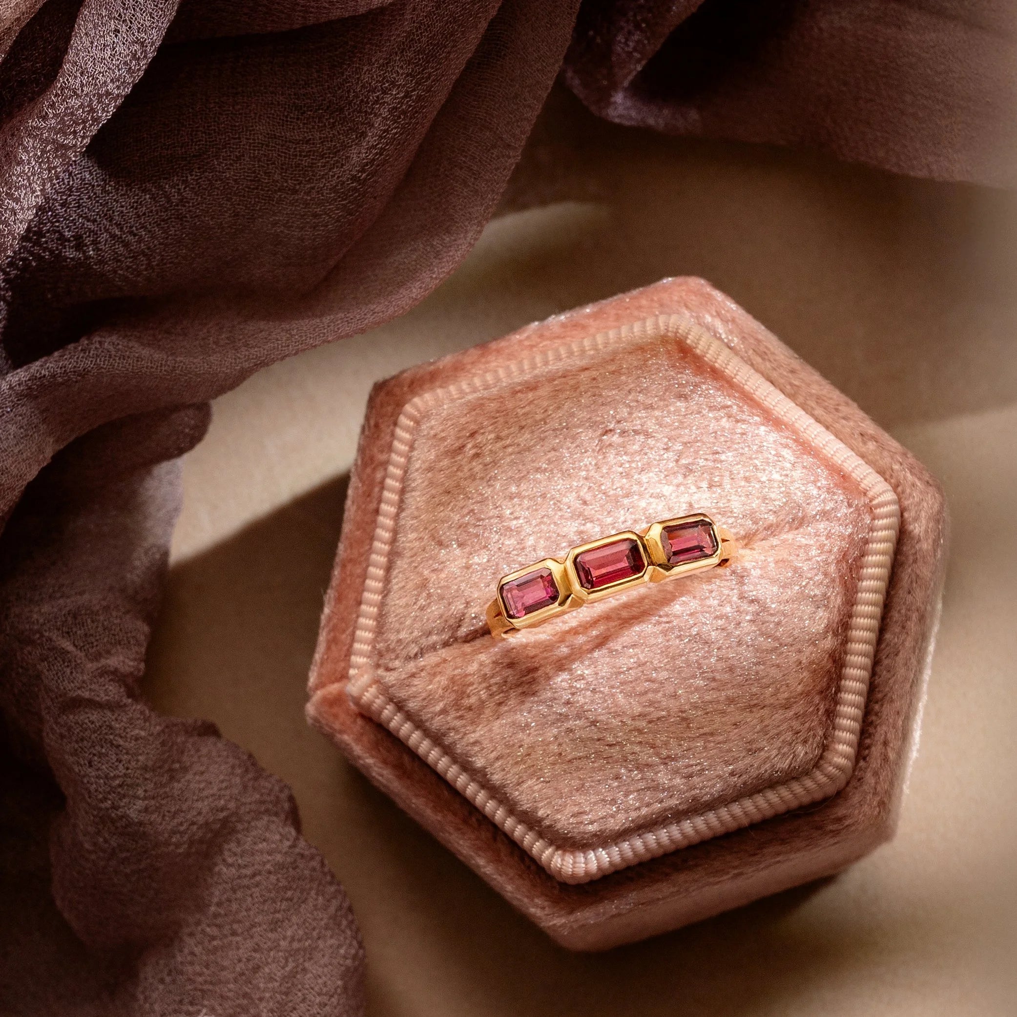 Gold ring with purple gemstones in a pink jewelry box on a soft fabric background