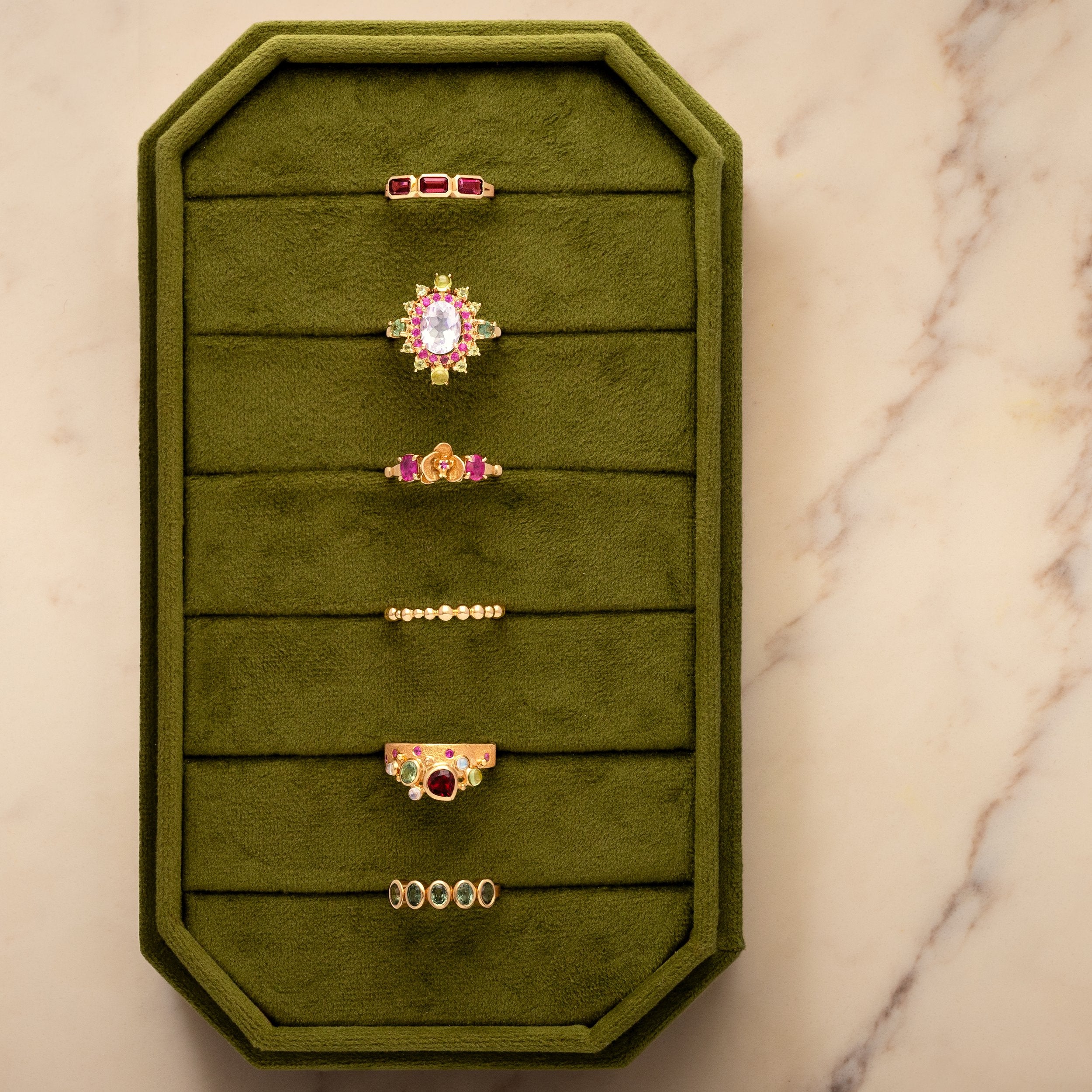 Green jewelry display with various rings on a marble surface