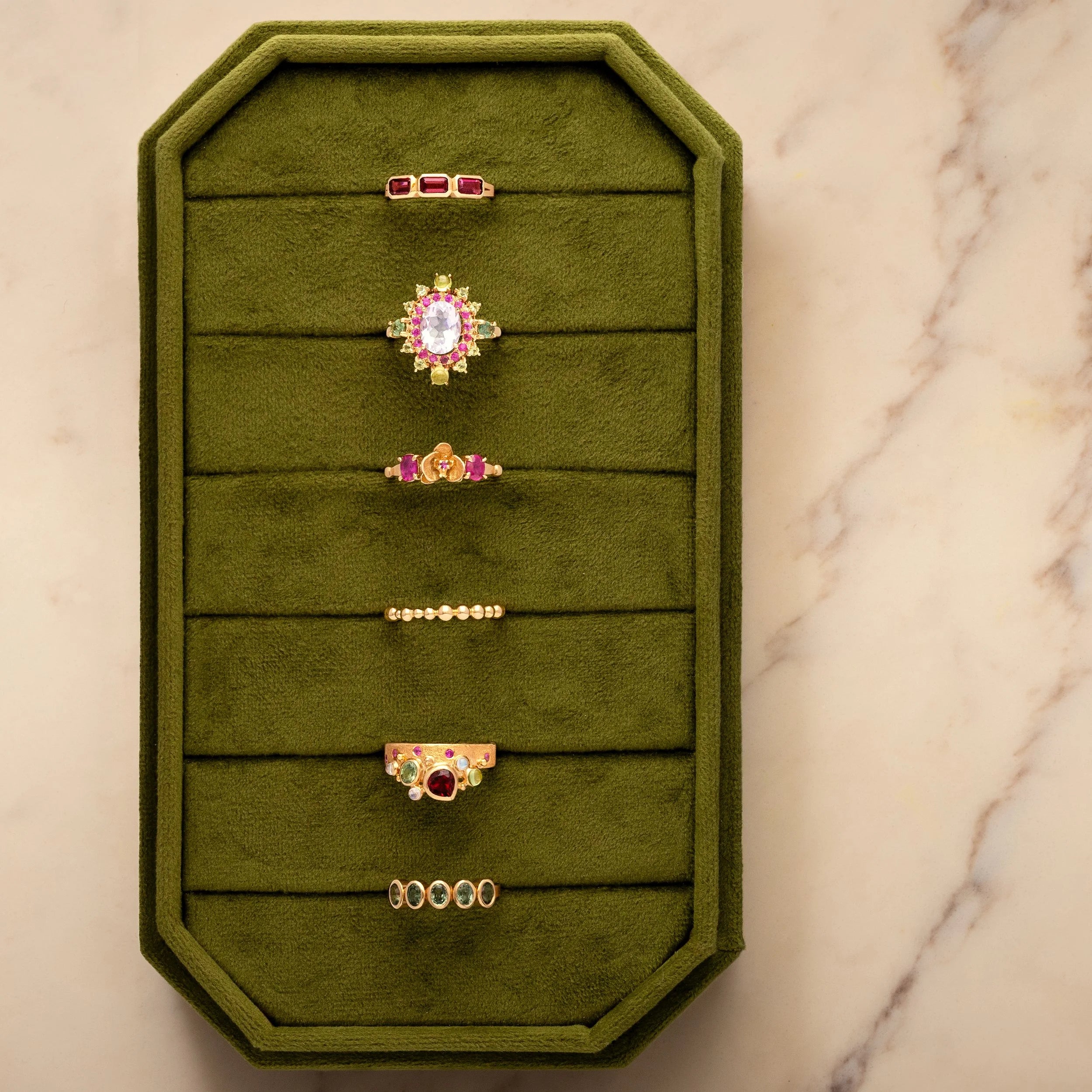 Green jewelry display with various rings on a marble surface