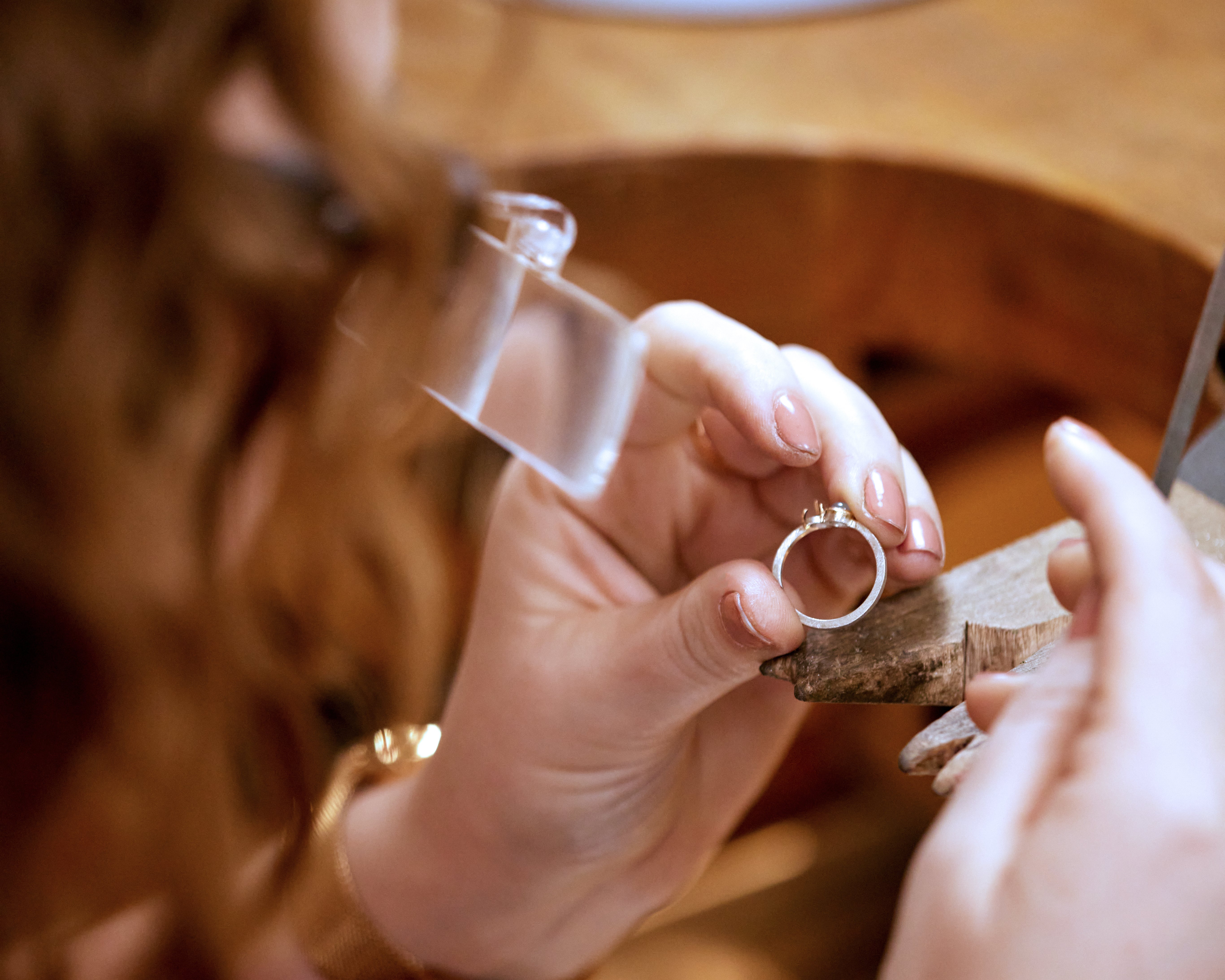 Jeweler holding a ring with a wooden anvil in a workshop setting