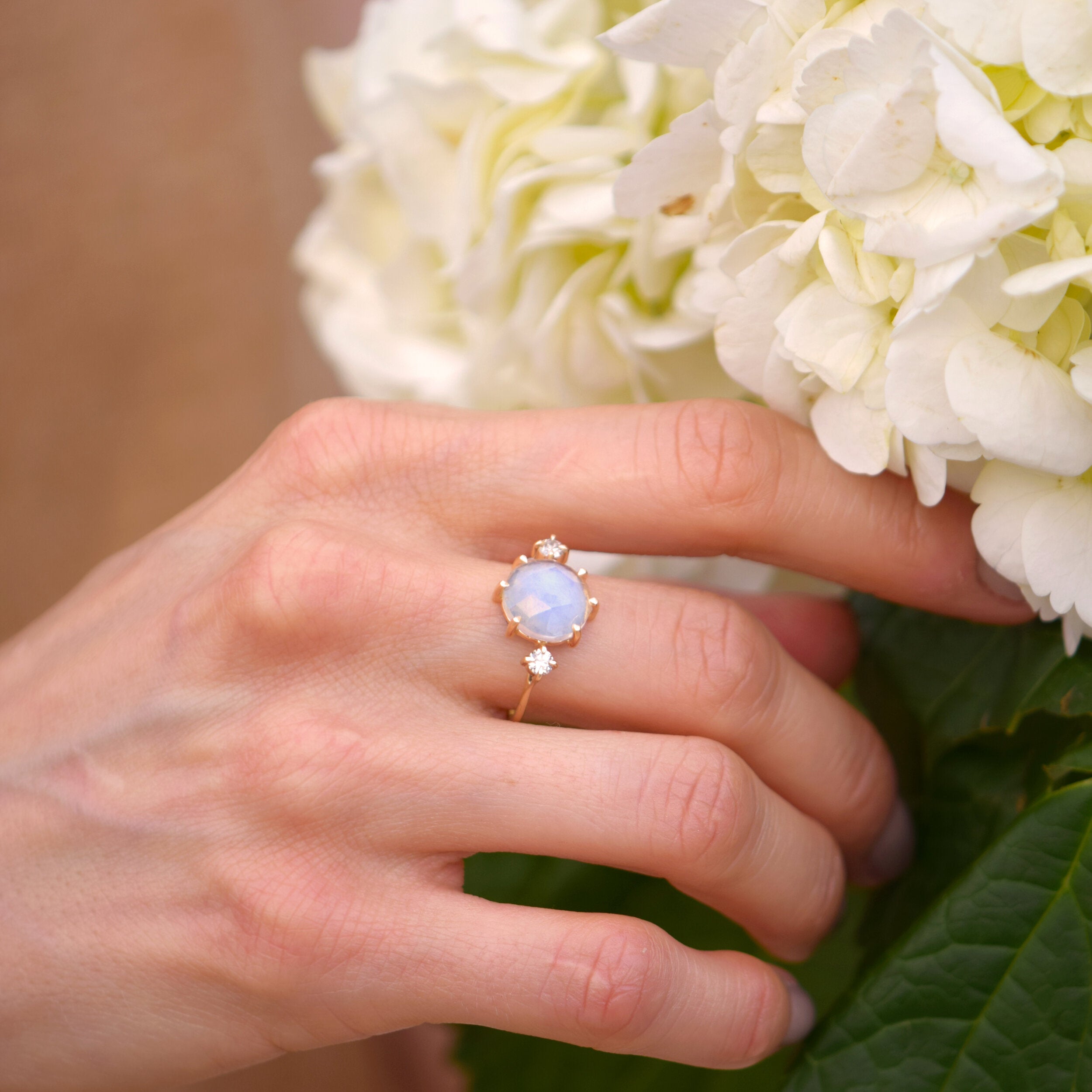 Hand wearing a ring with a moonstone against a background of white flowers