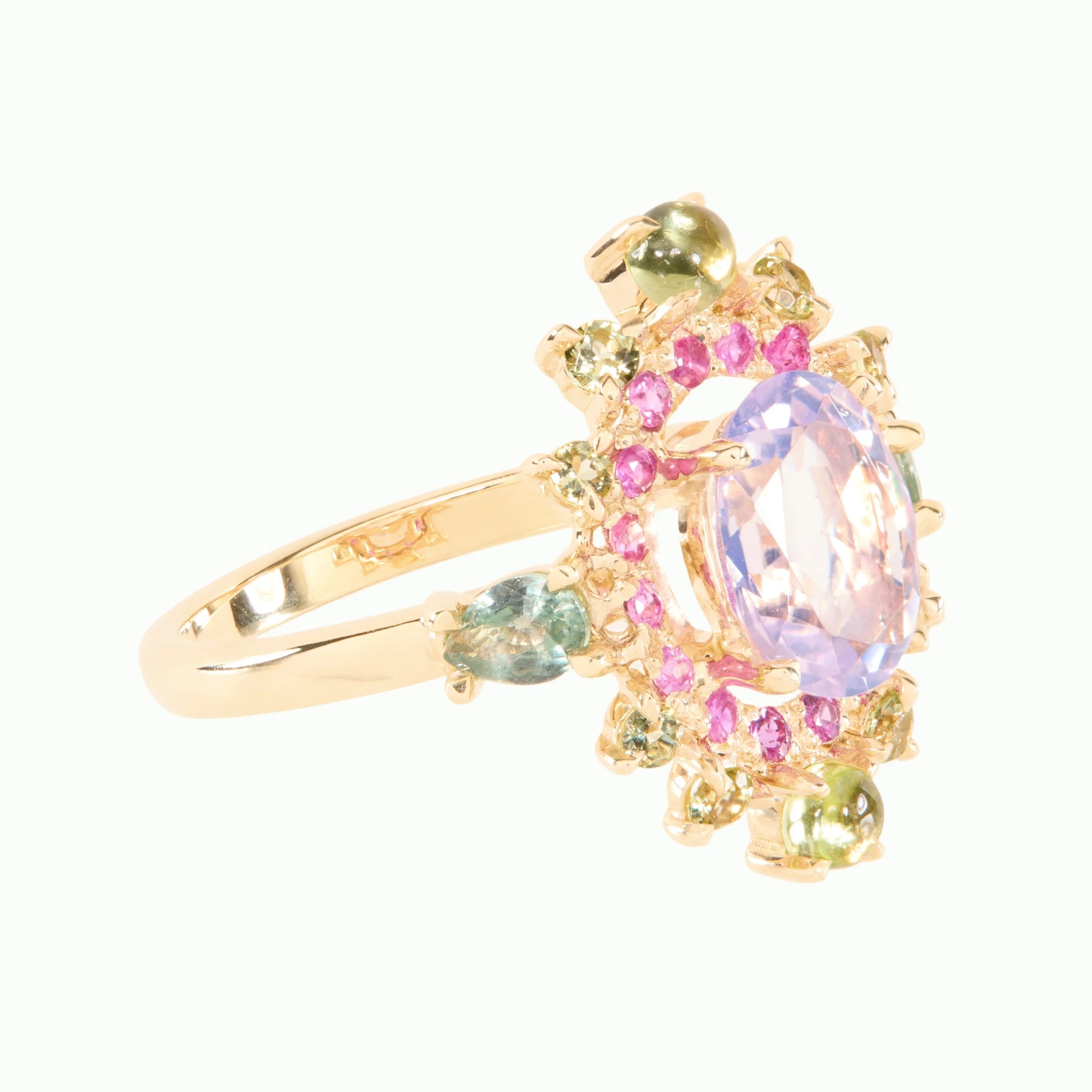 A gold ring featuring a large oval light purple center stone surrounded by small pink and green gemstones, set on a plain white background.