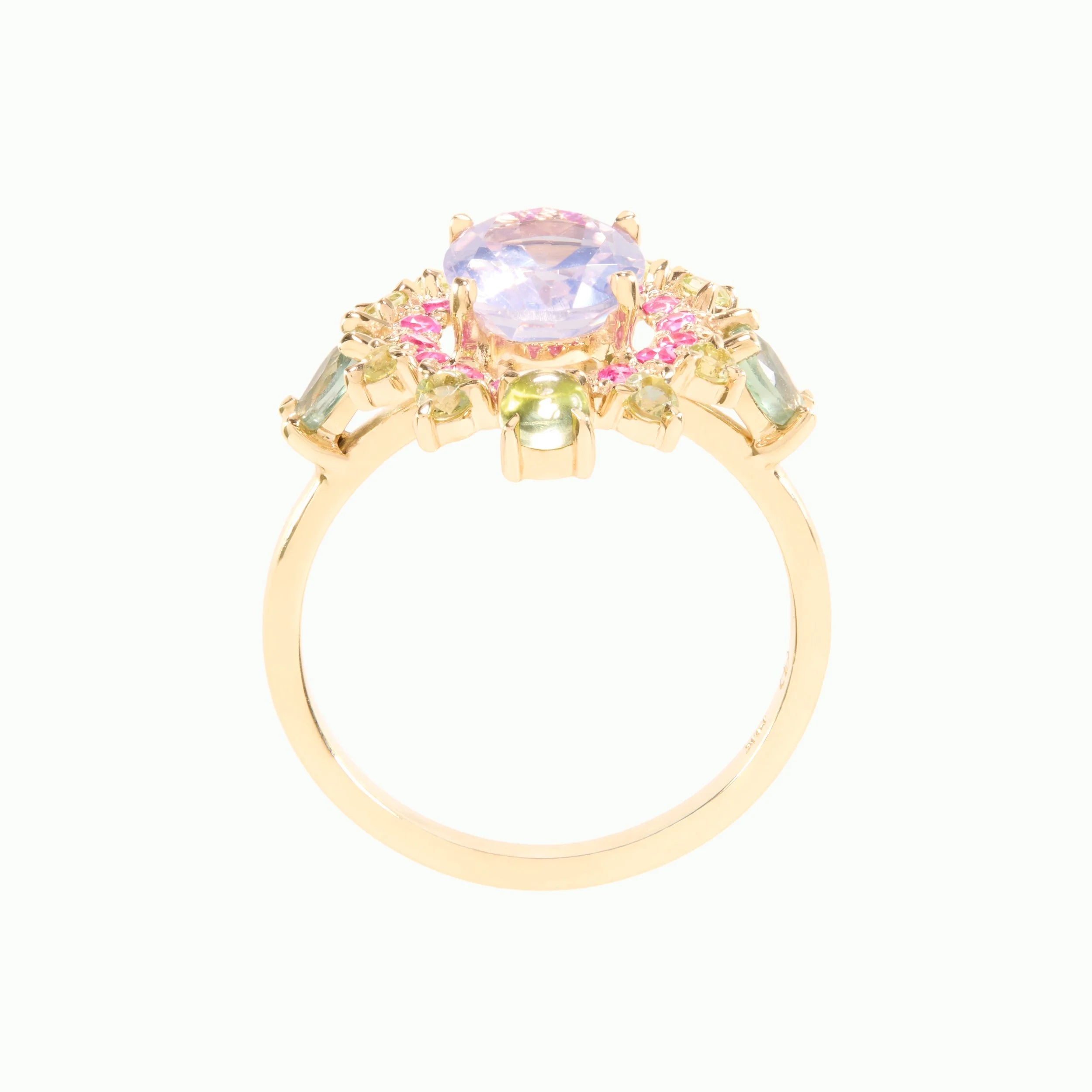 A gold ring featuring a large oval light purple center stone surrounded by small pink and green accent stones, set on a plain white background.