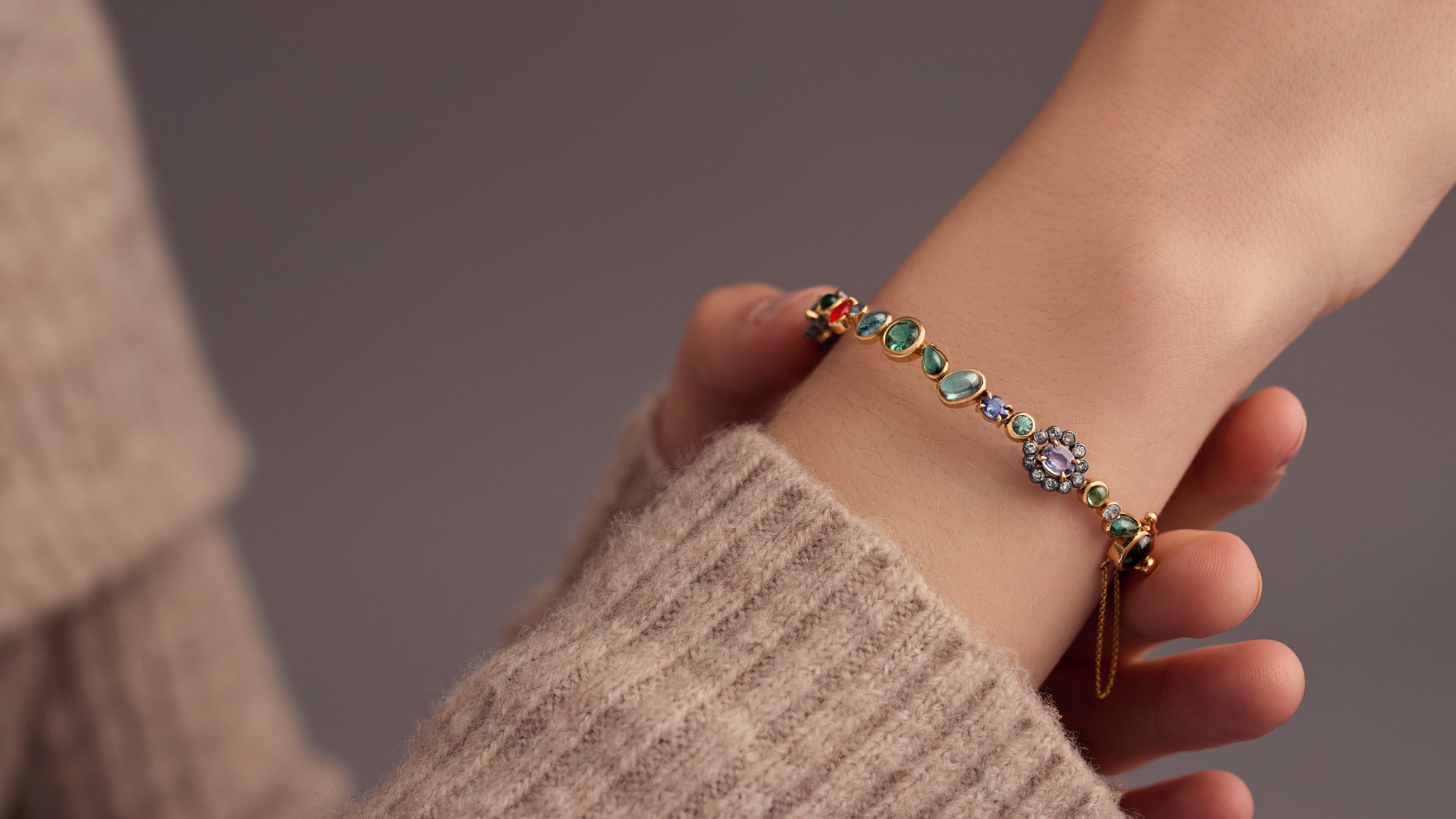 Woman wearing multi-gemstone hinged bracelet in blue and orange on neutral background