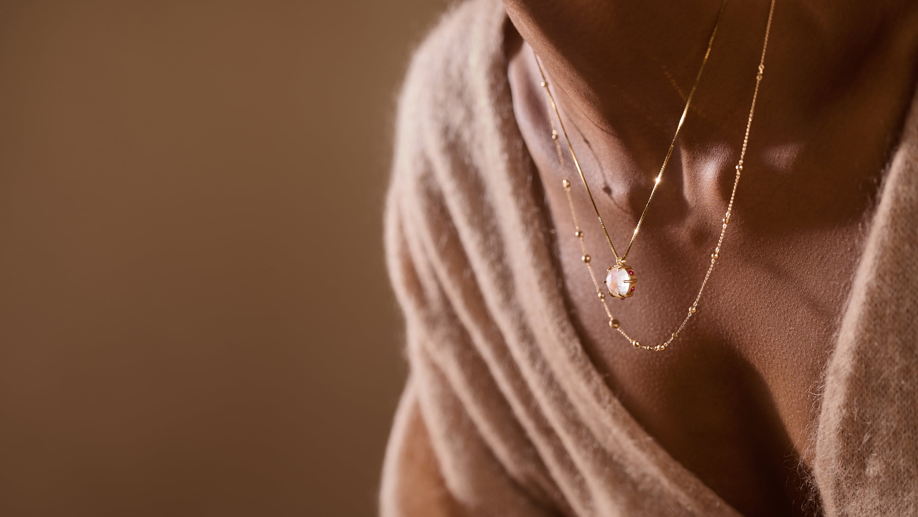 Woman wearing layered gemstone necklaces on brown background