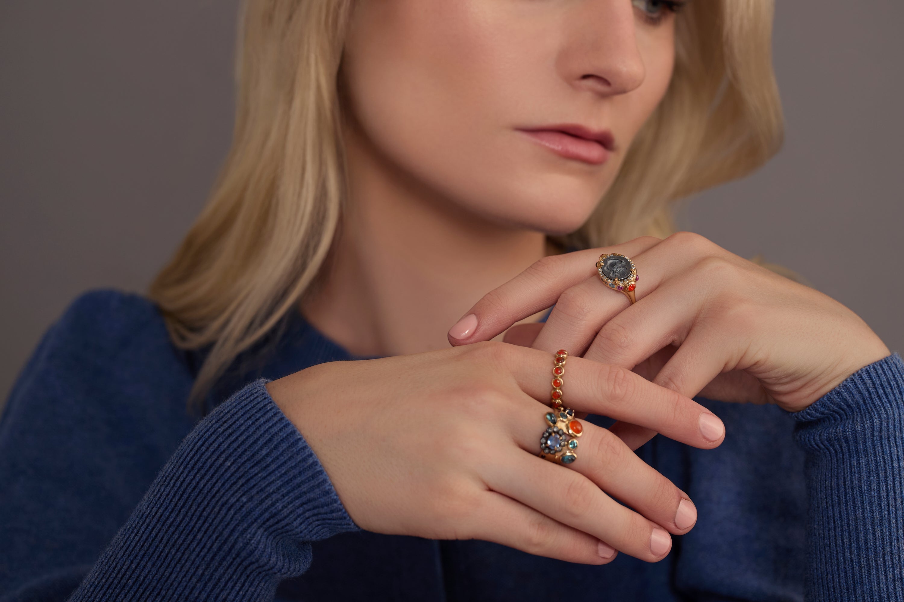 Woman wearing multiple colorful gemstone rings in blue sweater
