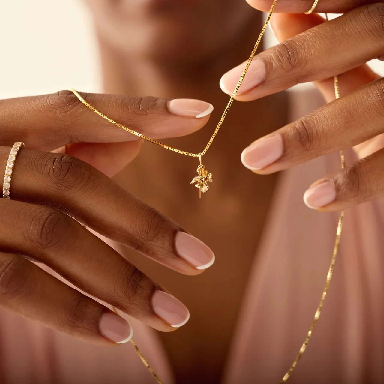 Close-up of hands holding a gold necklace with a delicate pendant against a blurred background
