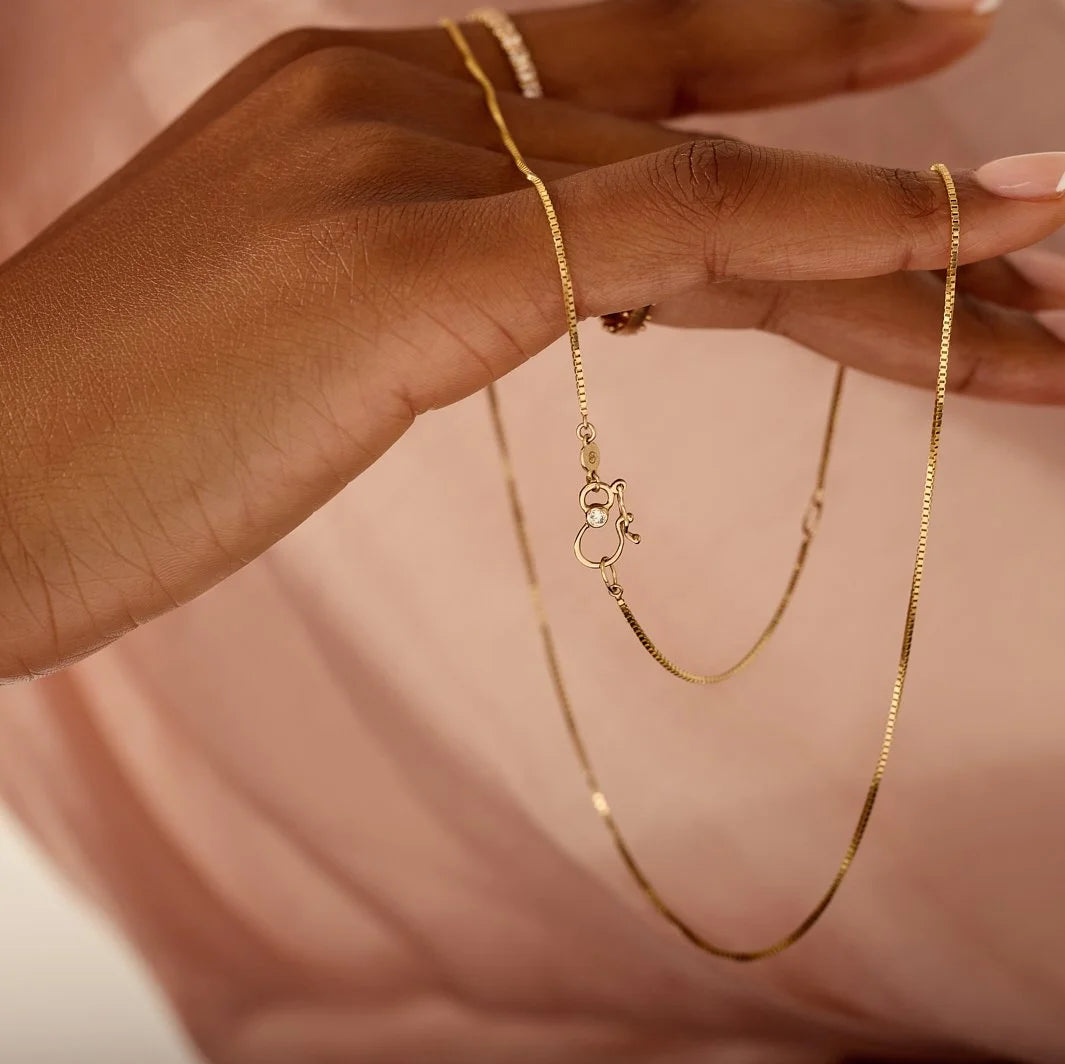 Gold chain necklace held by a hand against a neutral background