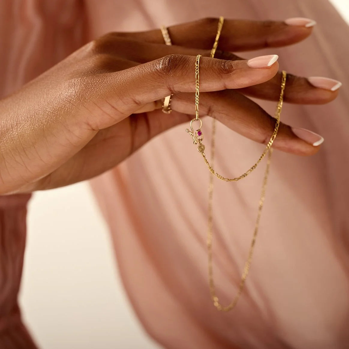 Close-up of hands wearing gold jewelry on a soft pink background