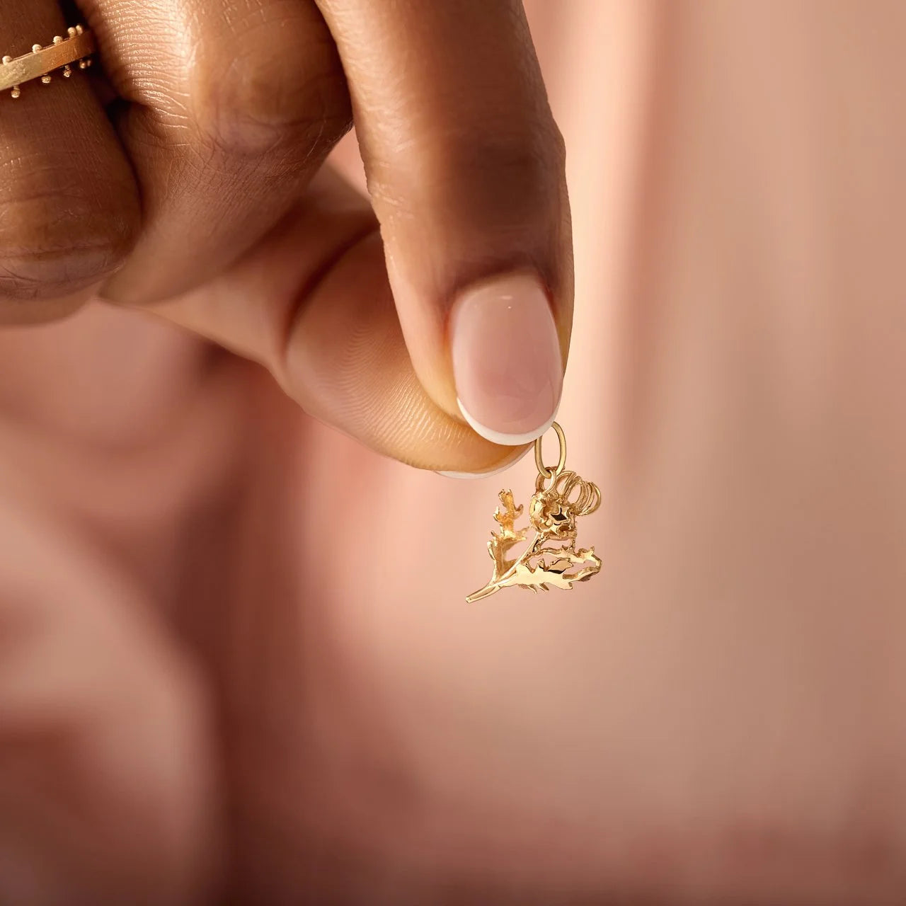 Gold charm held between fingers against a blurred background