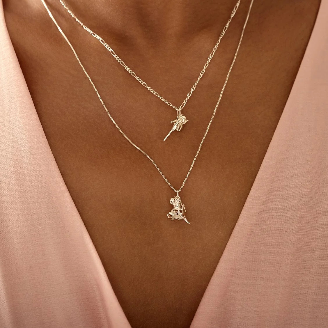 Two gold necklaces with small pendants on a person wearing a pink top.