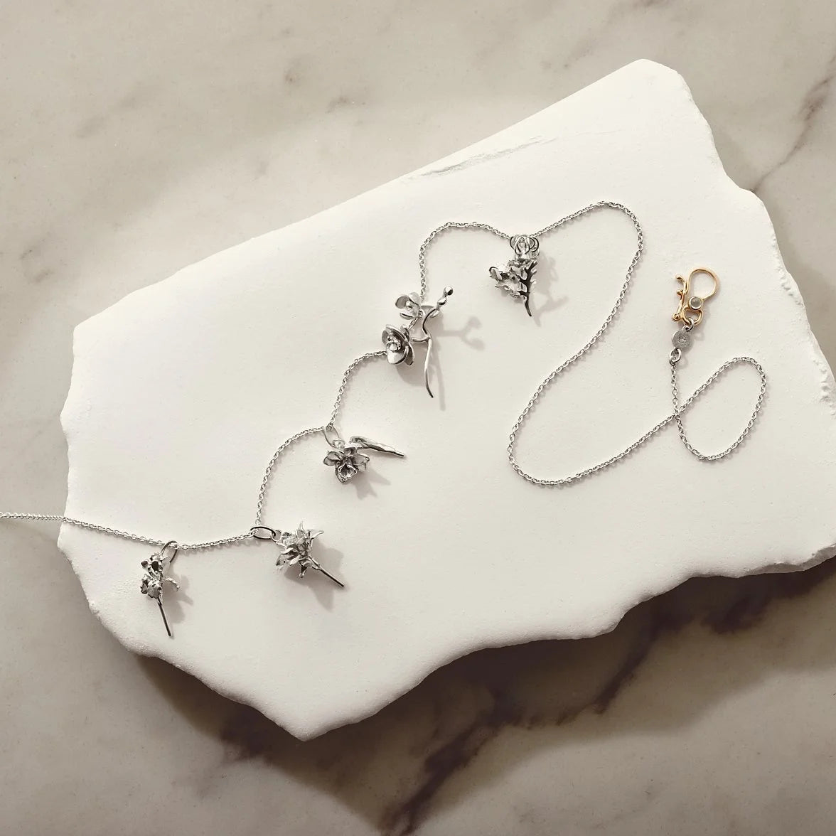 Silver necklace with floral pendants on a white stone surface