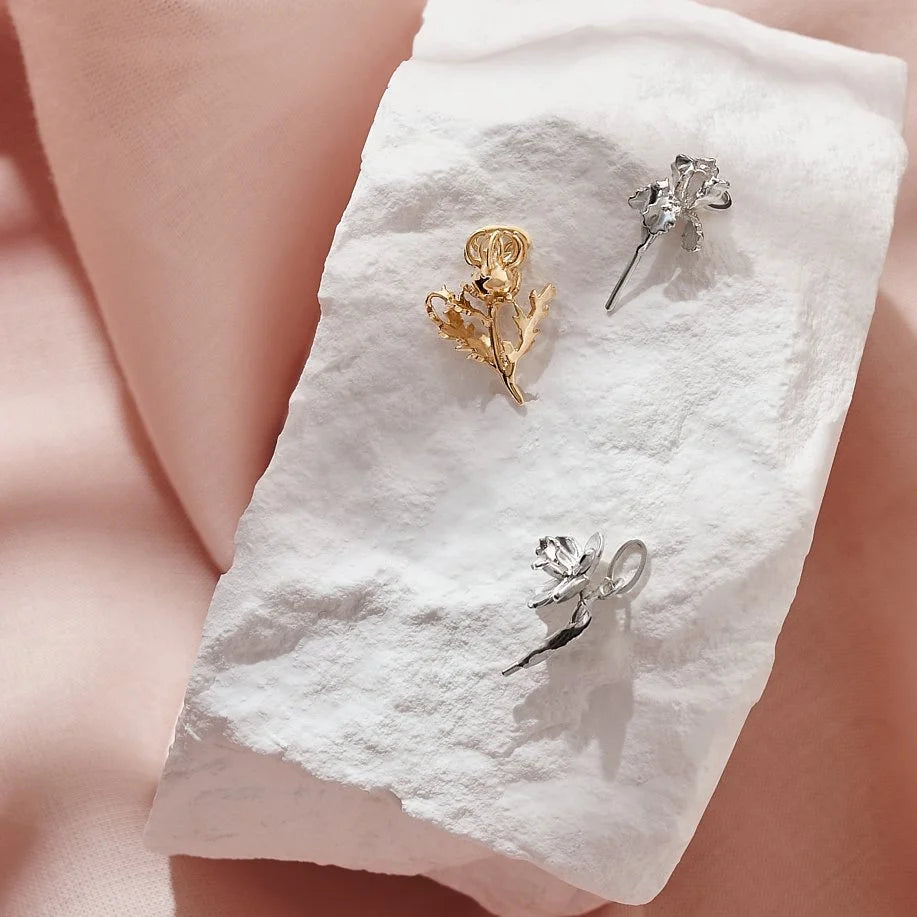 Three pairs of floral charms on a white cloth with a soft pink background