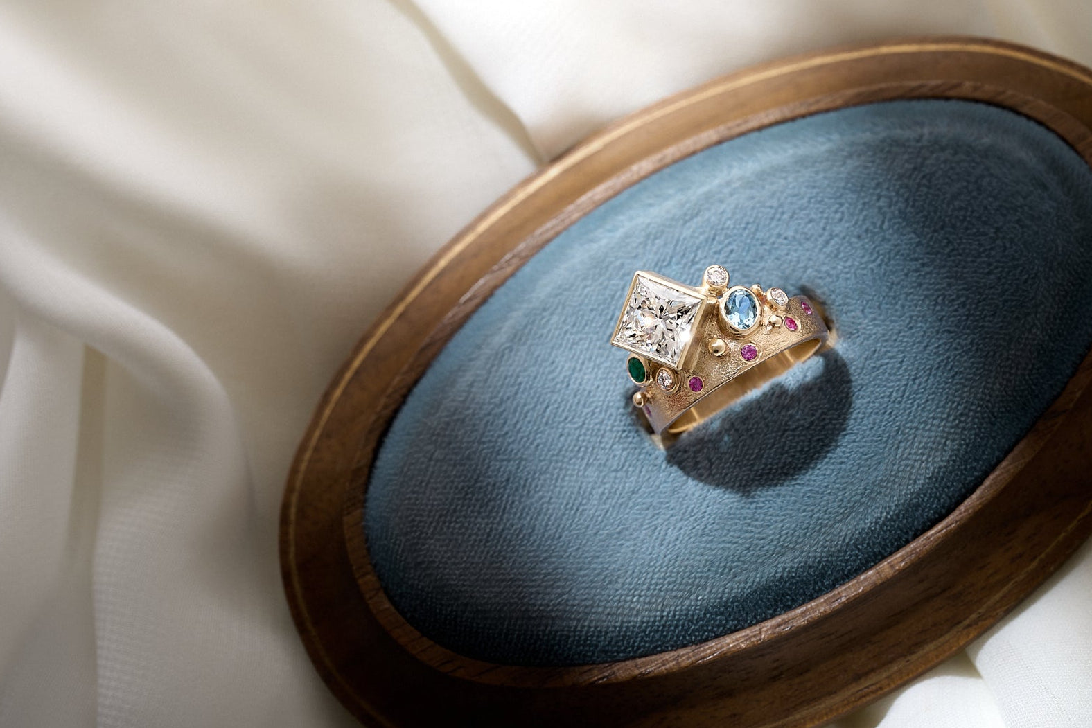 Elegant ring with gemstones on a blue cushion inside a wooden box