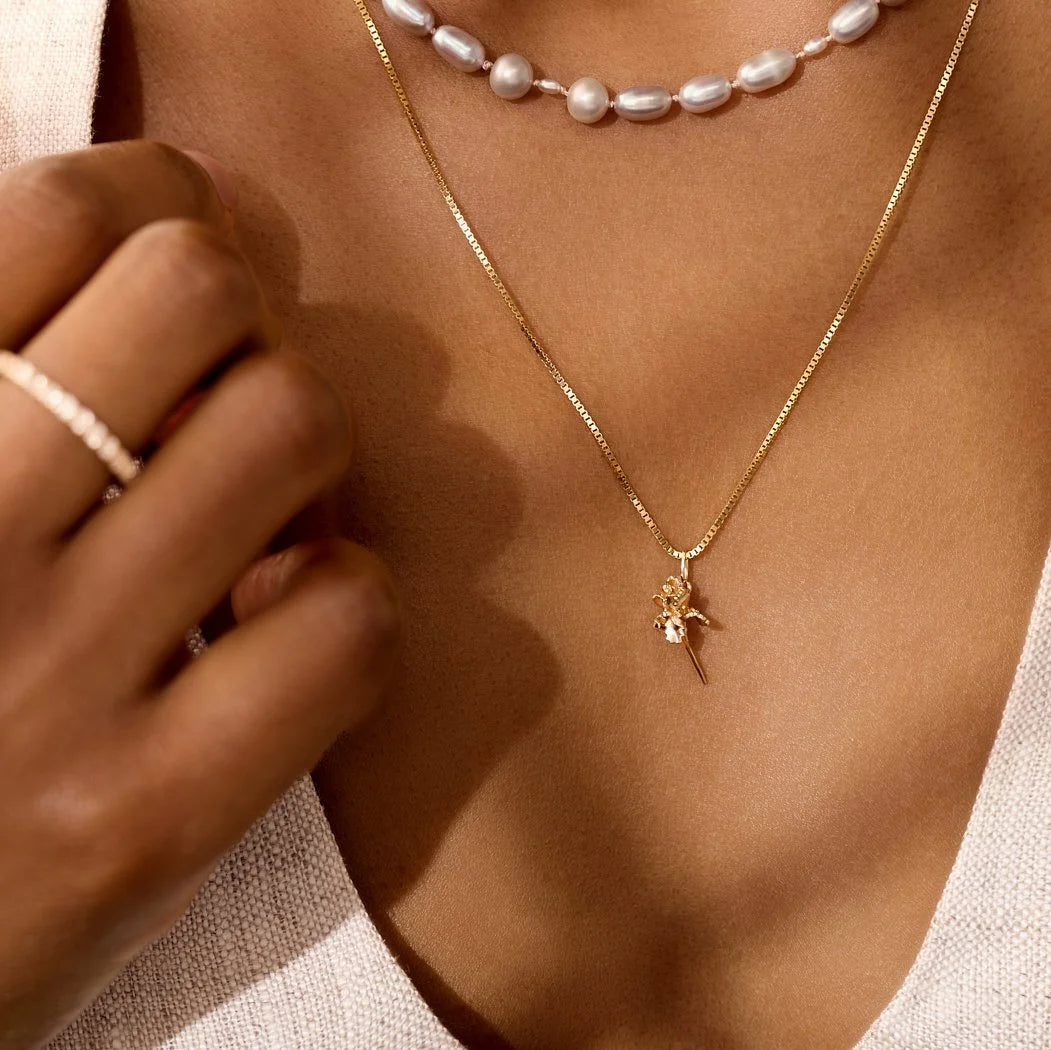 Close-up of a person wearing a gold necklace with an iris pendant and a pearl necklace.