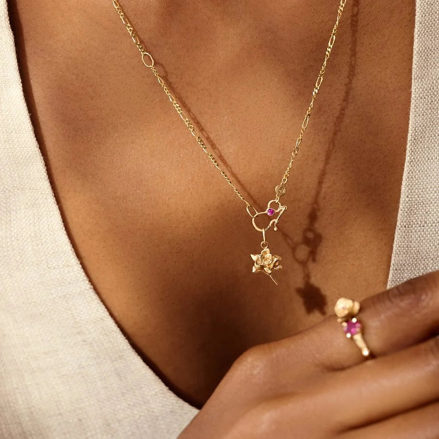 Gold necklace and ring with floral design and pink gemstones on a person's neck and hand.
