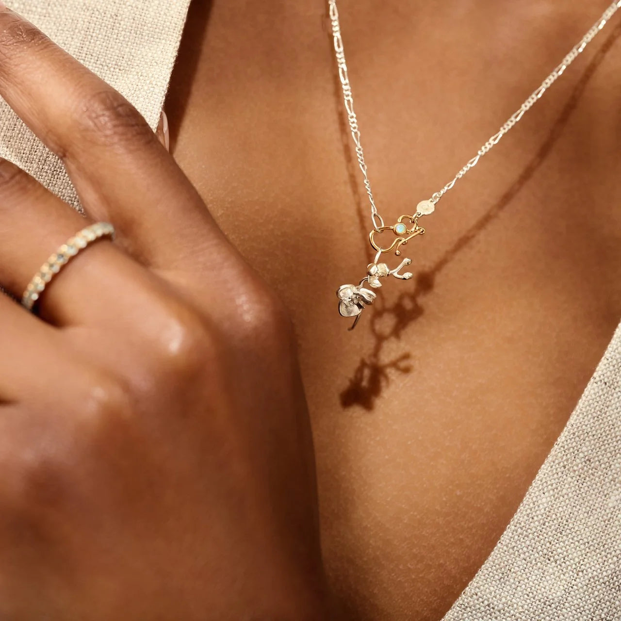 Close-up of a hand wearing a gold ring and holding a silver necklace with a pendant.