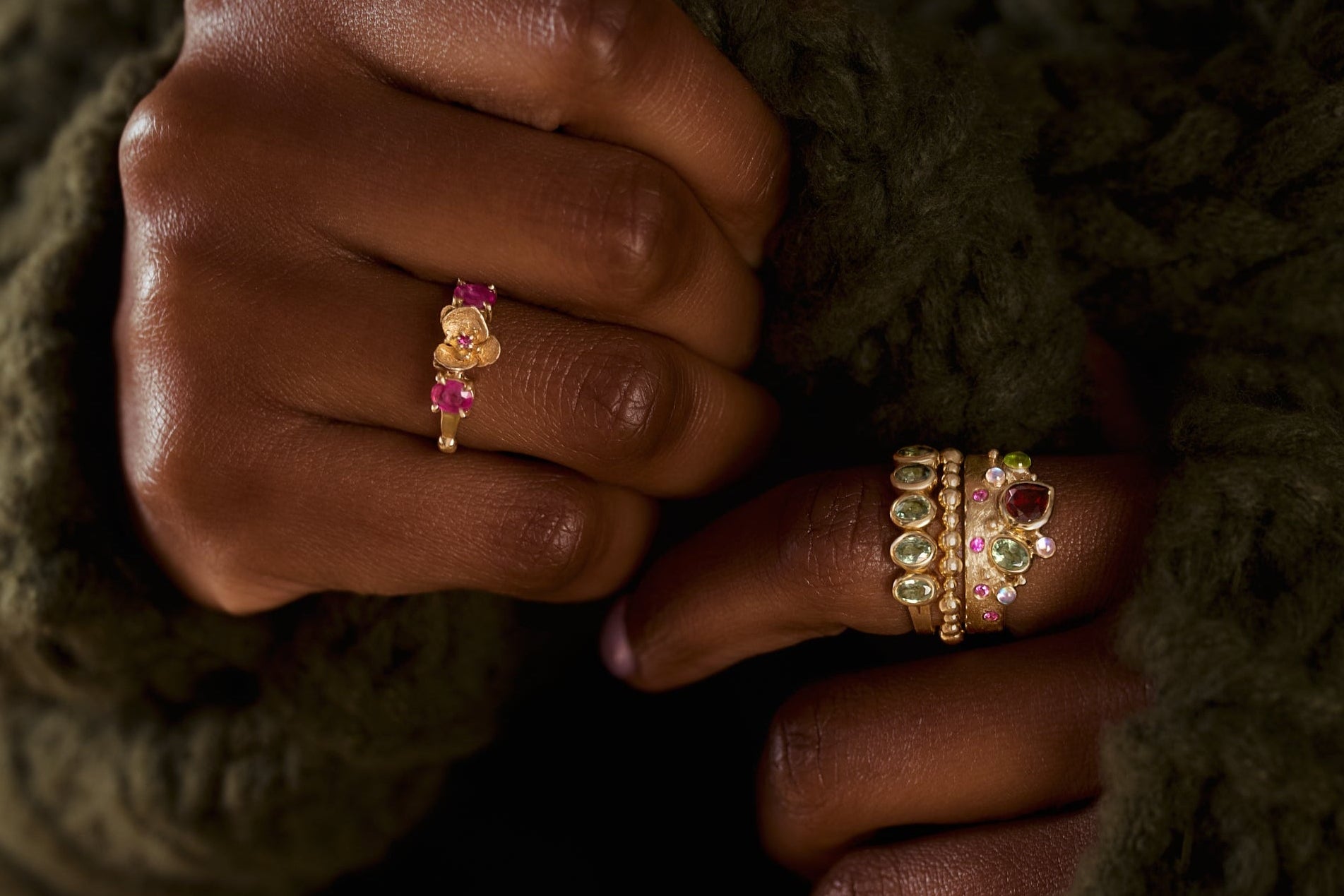 Close-up of hands wearing gold rings with gemstones against a textured green sweater.