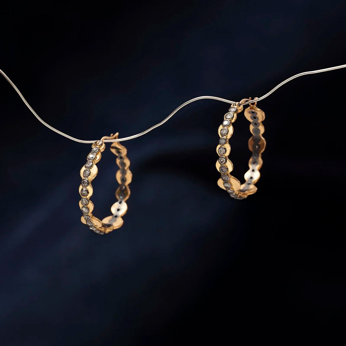 Gold hoop earrings hanging on a dark background