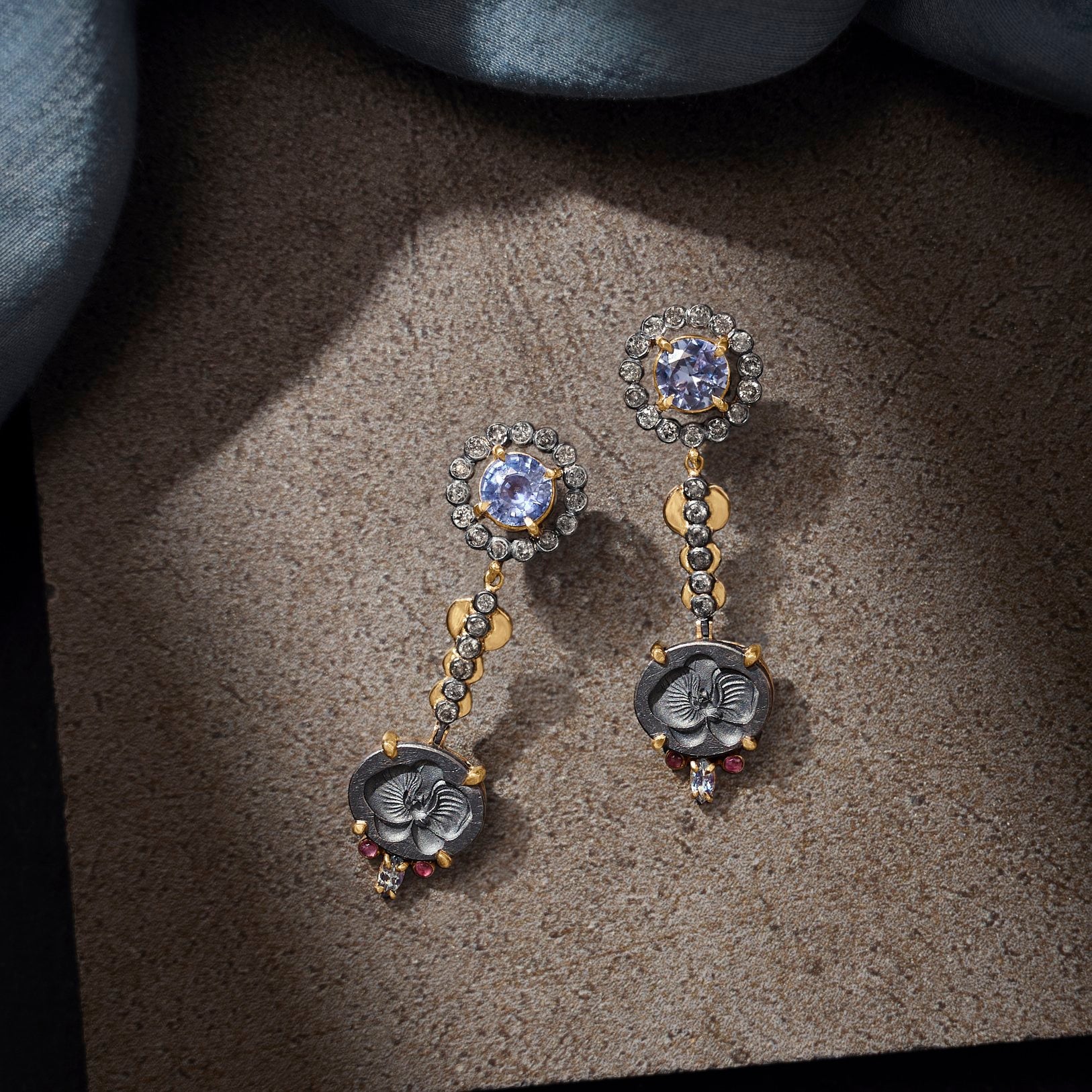 Pair of ornate earrings with gemstones on a textured surface