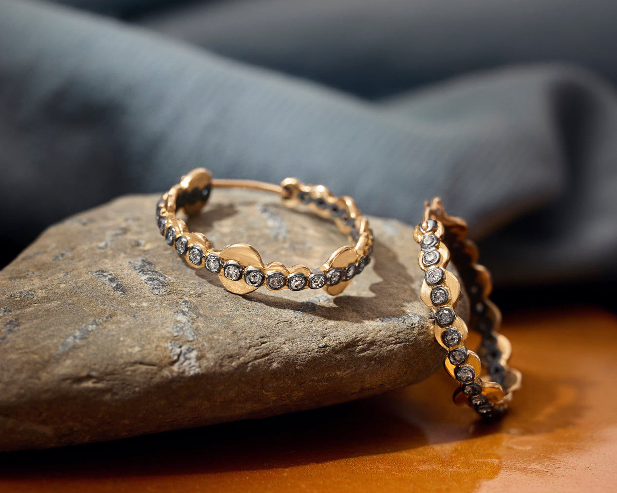 Gold hoop earrings with embedded diamonds on a stone surface with a gray fabric background
