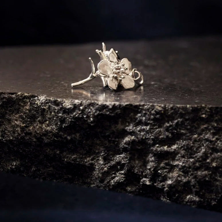 Silver floral earring on a dark stone surface