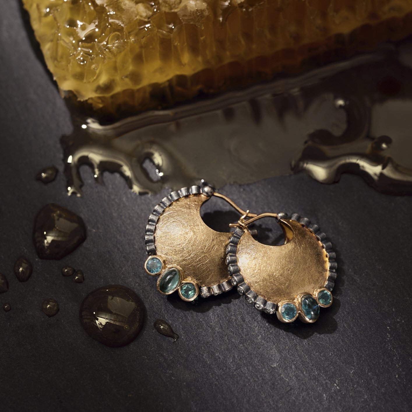 Gold earrings with gemstones on a dark surface with honeycomb and honey.