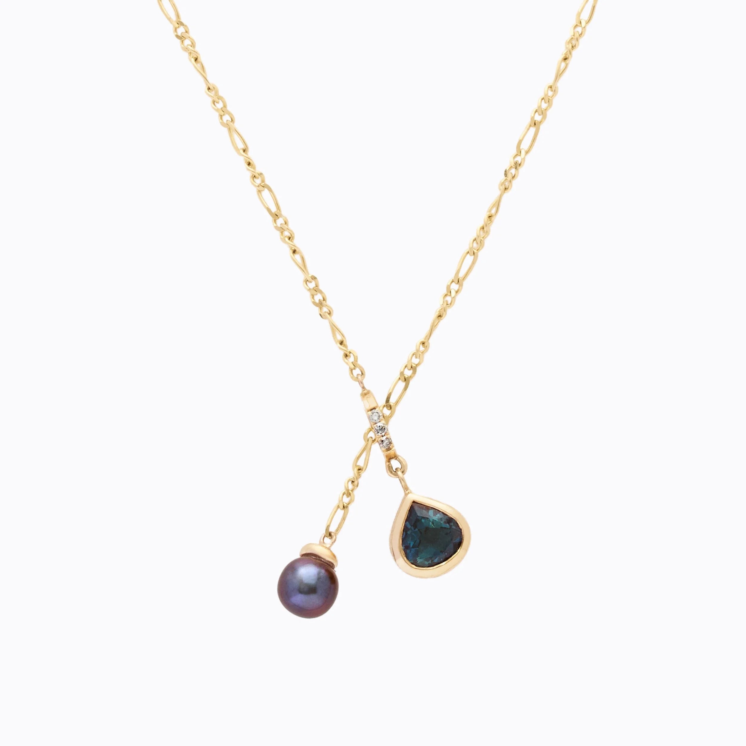 Gold necklace with a black pearl and teal teardrop pendant on a white background