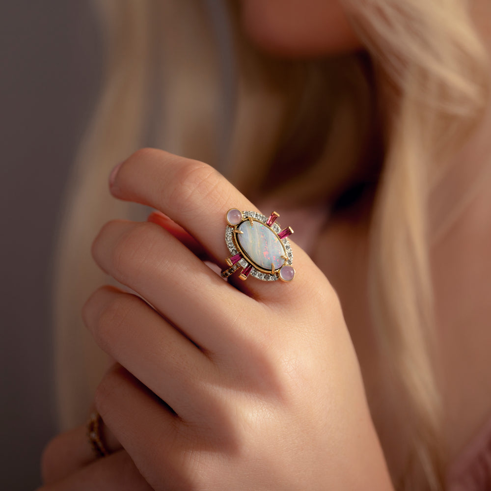 Close-up of a hand wearing an ornate ring with a pink gemstone against a neutral background